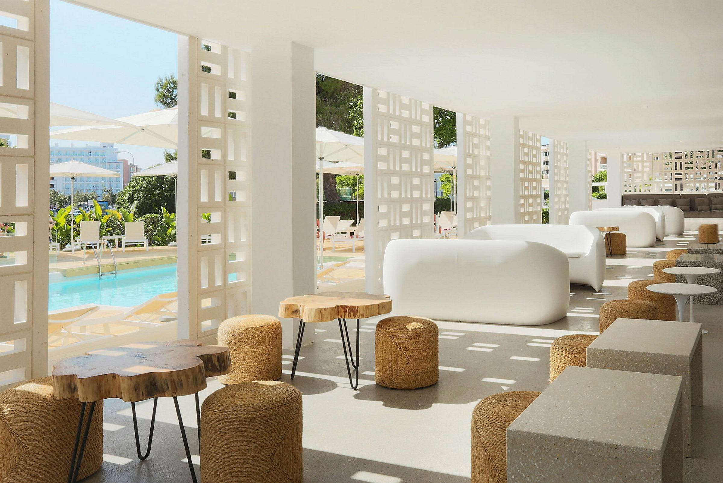 Moderne lounge med hvite sofaer og trebord, med utsikt mot et basseng og parasoller. (AI-generert tekst)