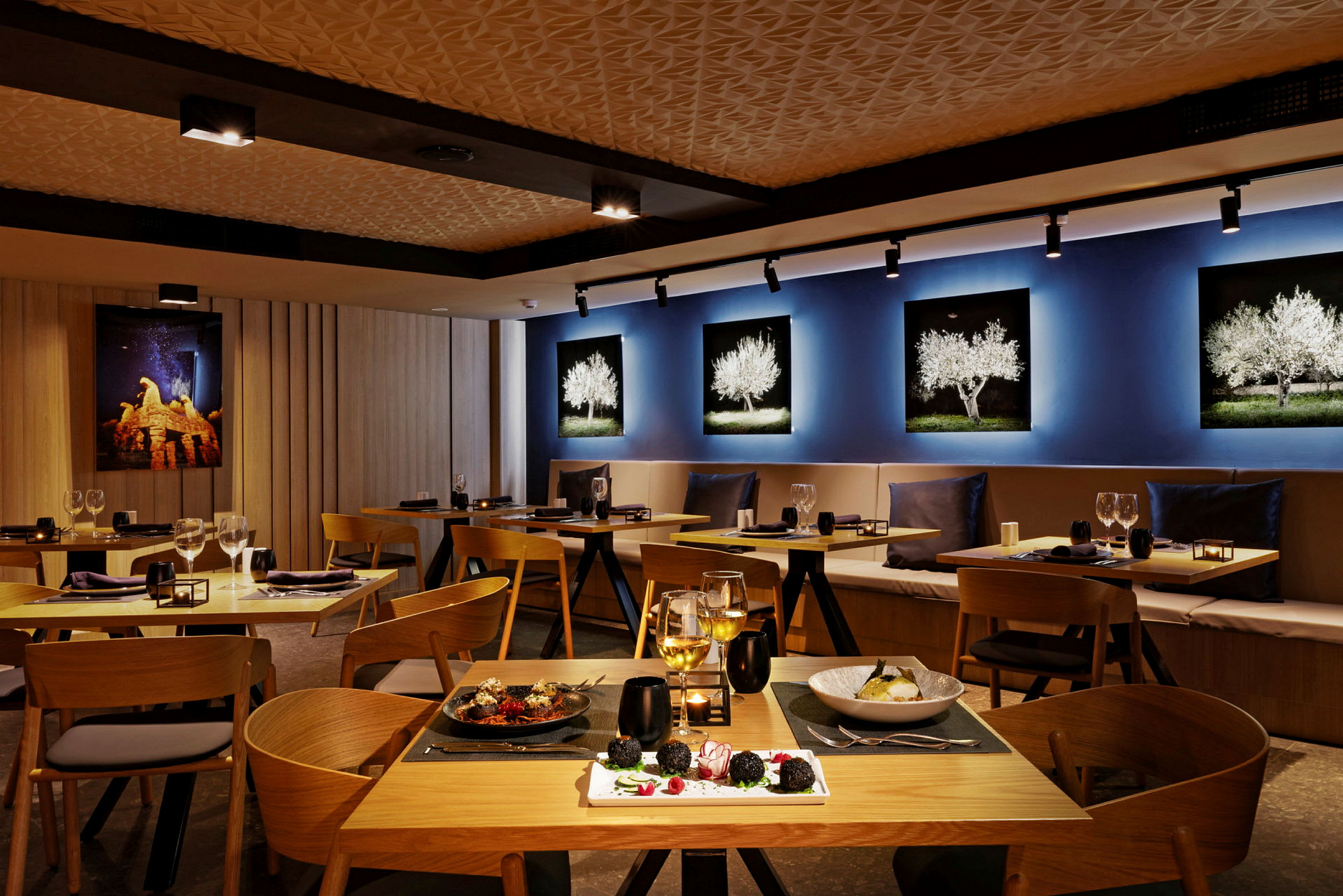 Interiør av en restaurant med trebord og stoler, dekorative veggbilder og servert mat på bordene. (AI-generert tekst)