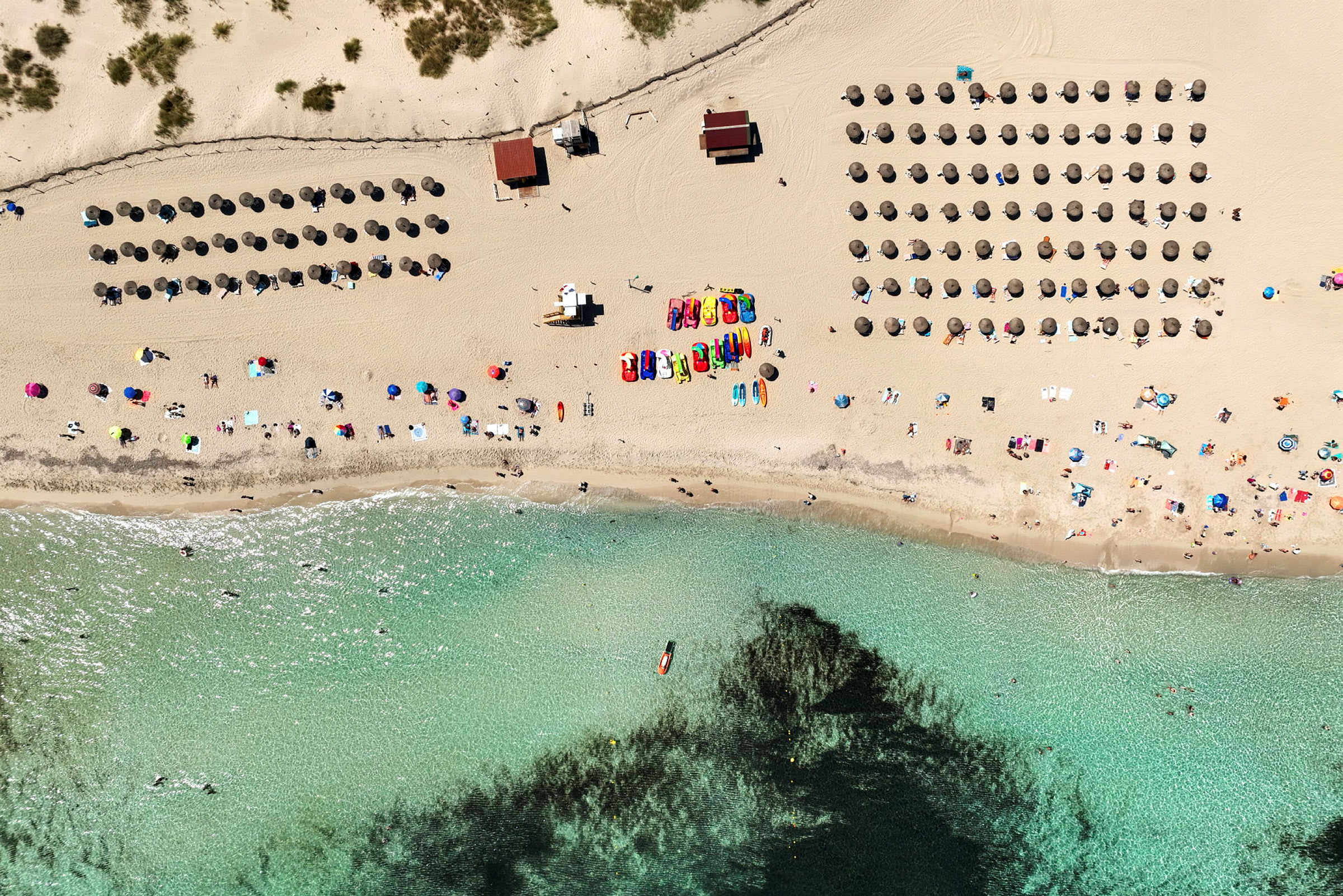 Luftfoto av en strand med parasoller, mennesker og klart vann. (AI-generert tekst)