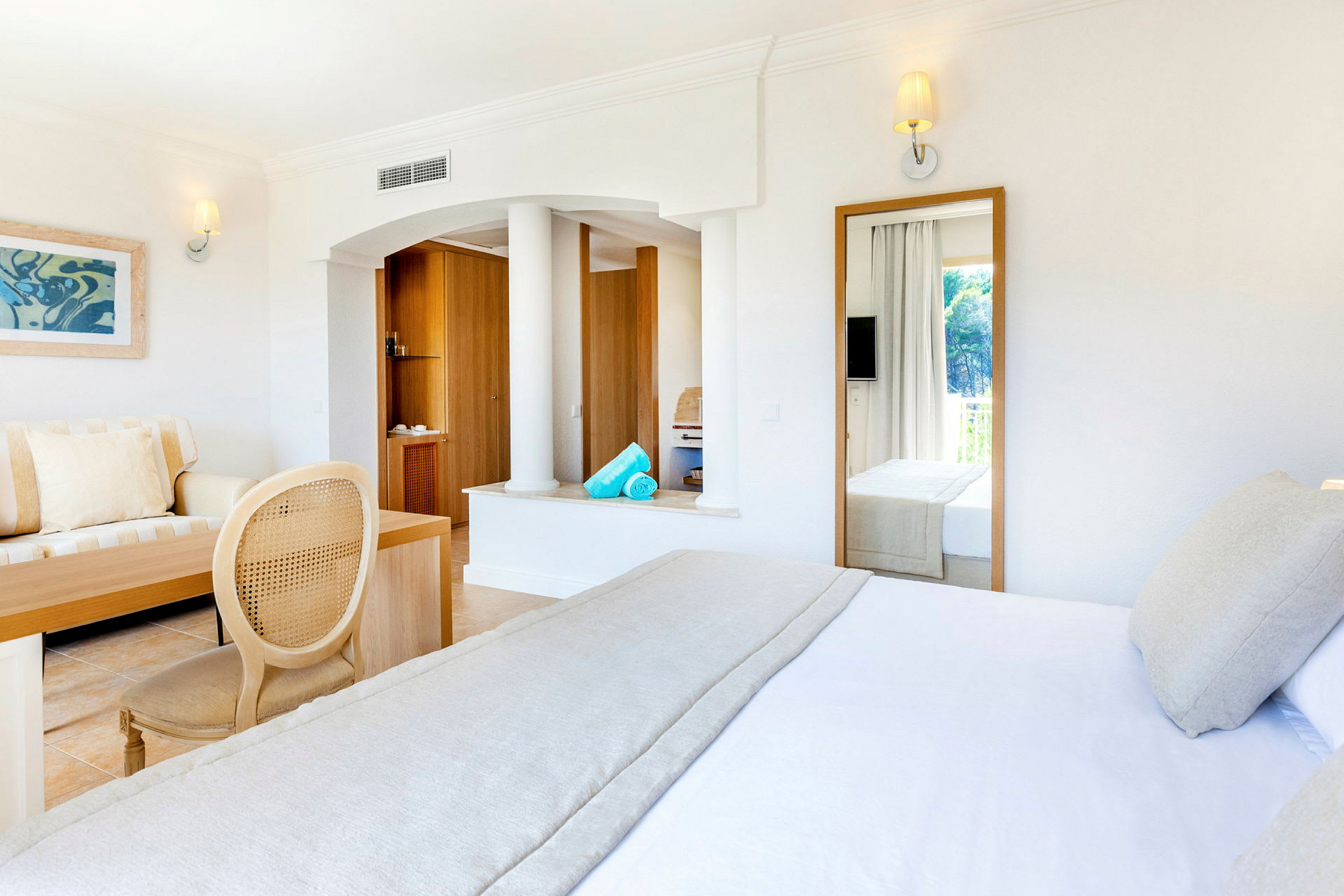 Lyst hotellrom med seng, sofa og store speil. (AI-generert tekst)