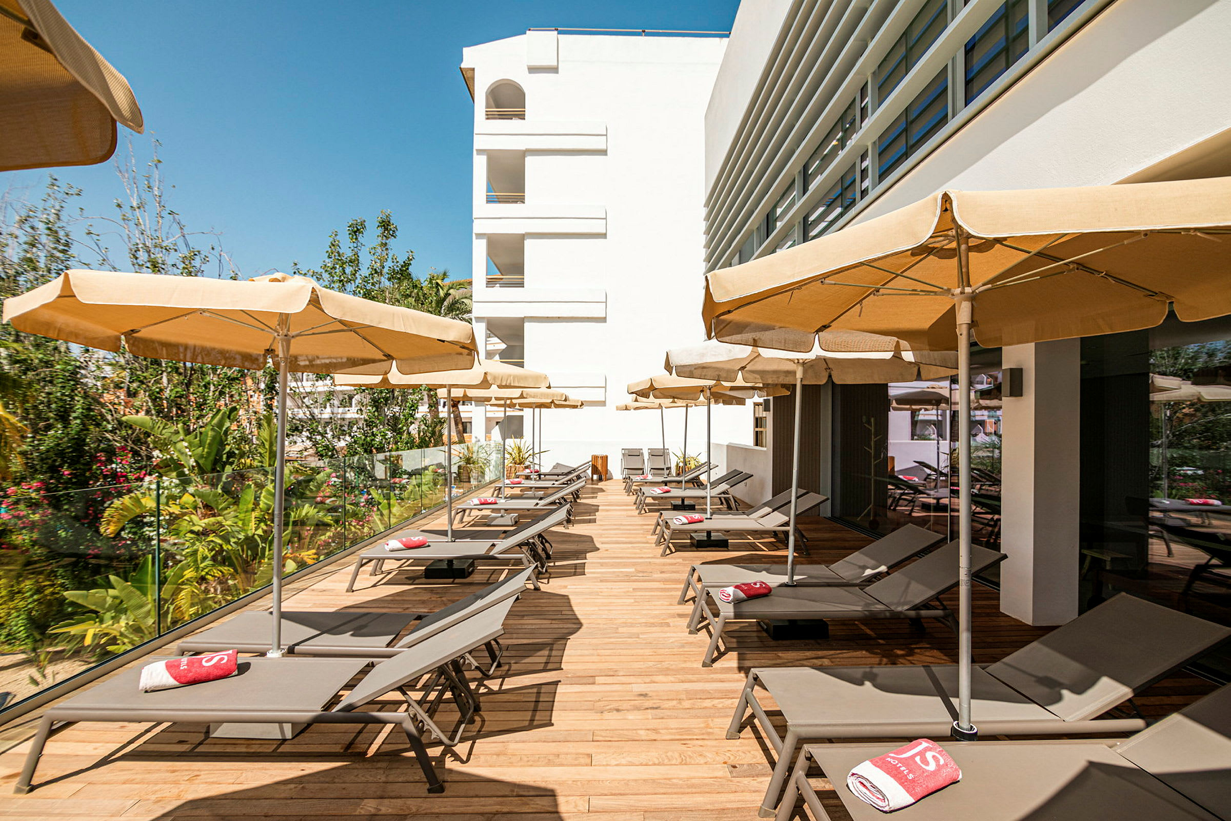 Solstoler med parasoller på en terrasse ved et hotellbygg. (AI-generert tekst)