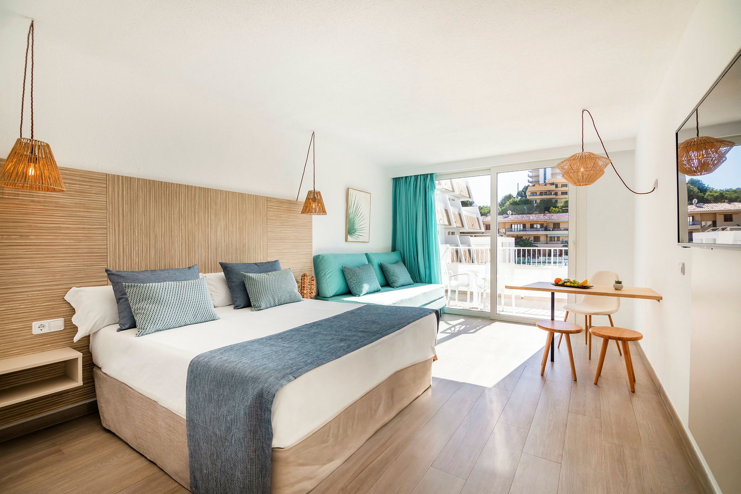 Hotellrom med en dobbeltseng, en sofa med puter, et lite spiseområde og en balkong. (AI-generert tekst)