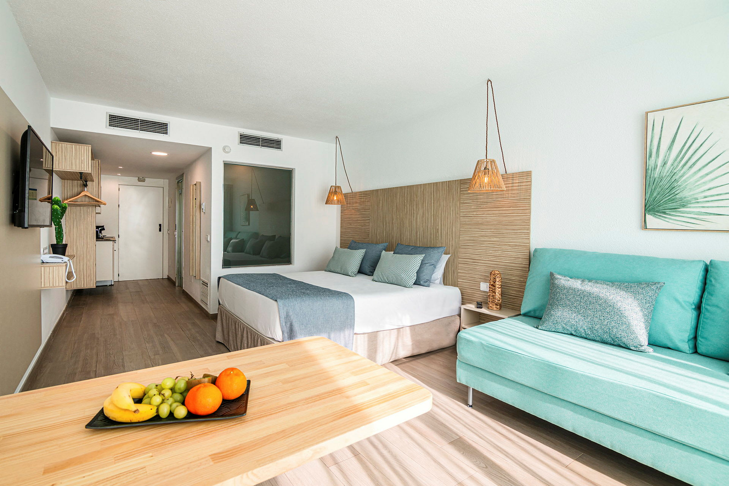 Hotellrom med seng, sofa og bord med frukt. (AI-generert tekst)