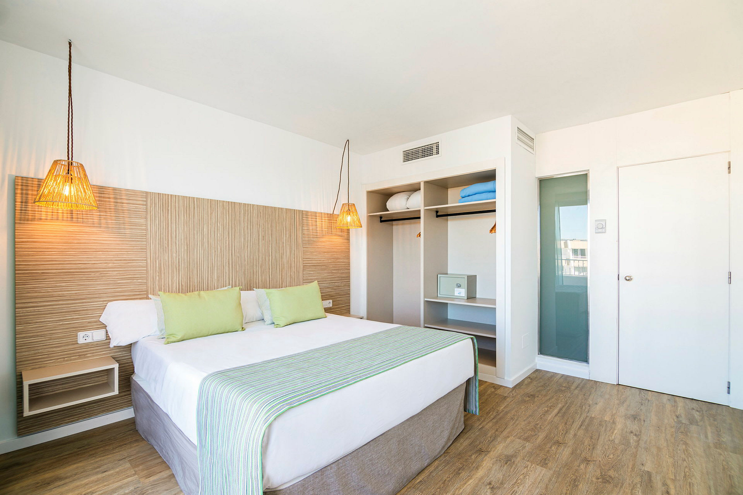 Et hotellrom med en dobbeltseng, lyse møbler og åpen garderobe. (AI-generert tekst)