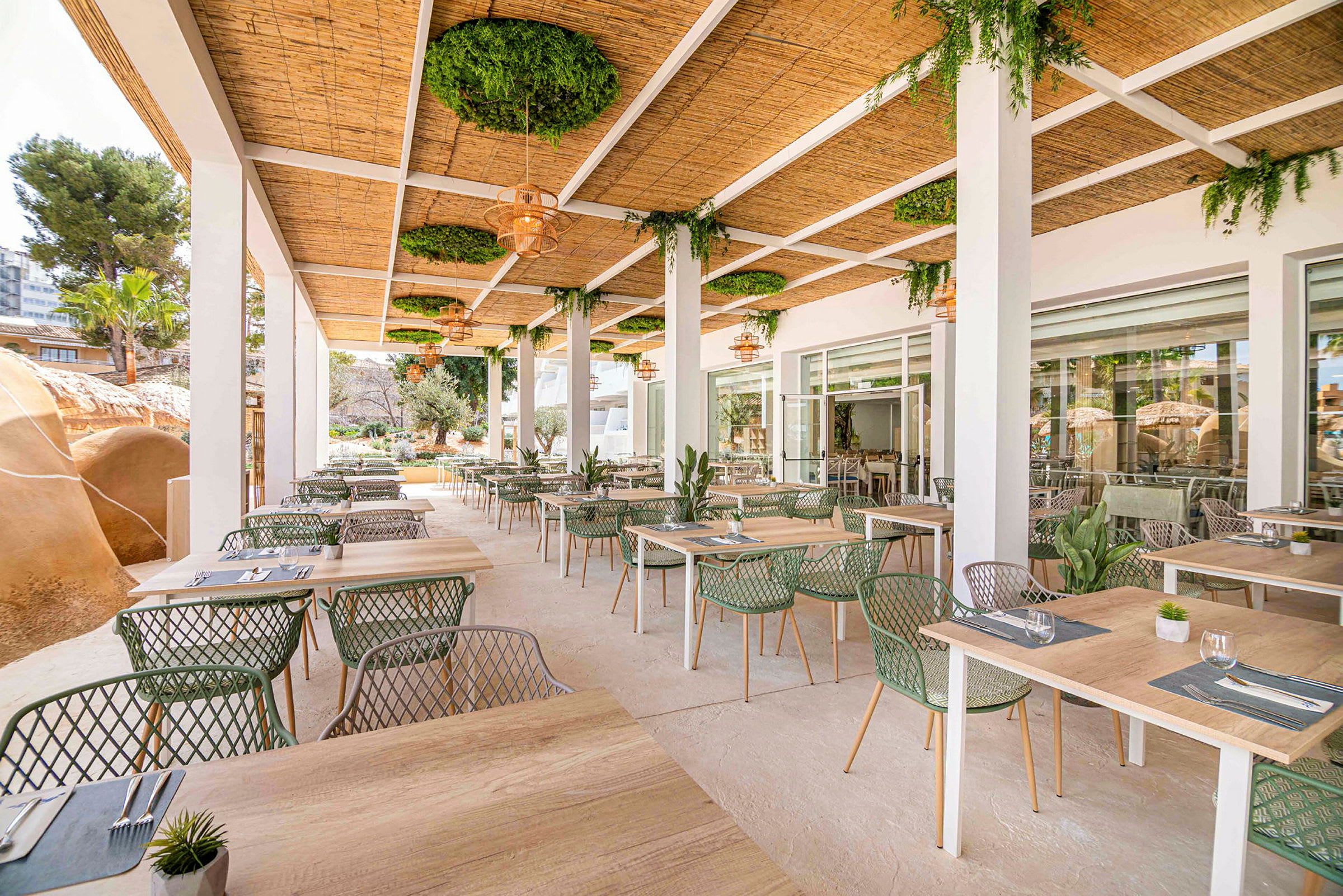Utendørsrestaurant med bord og stoler under et tak med grønne planter. (AI-generert tekst)