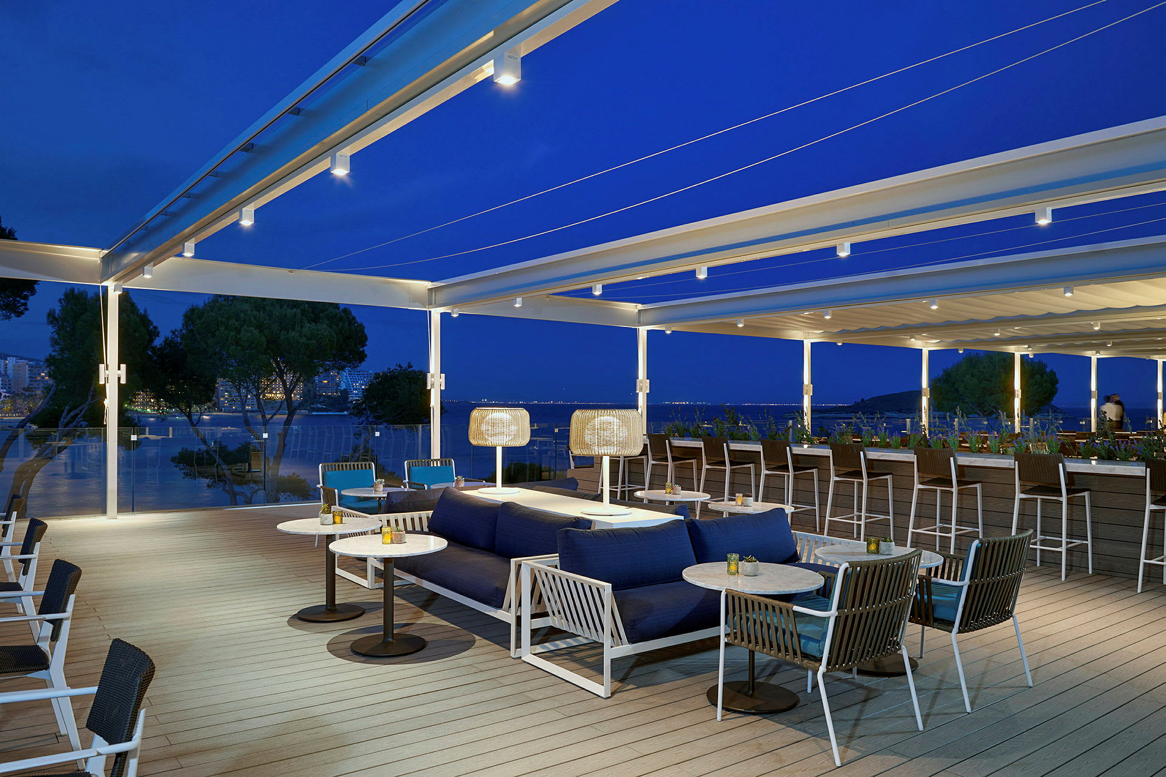 Bilde av en utendørs terrasse med sitteplasser og sofaer, plassert med en vakker utsikt over havet ved skumringen. (AI-generert tekst)