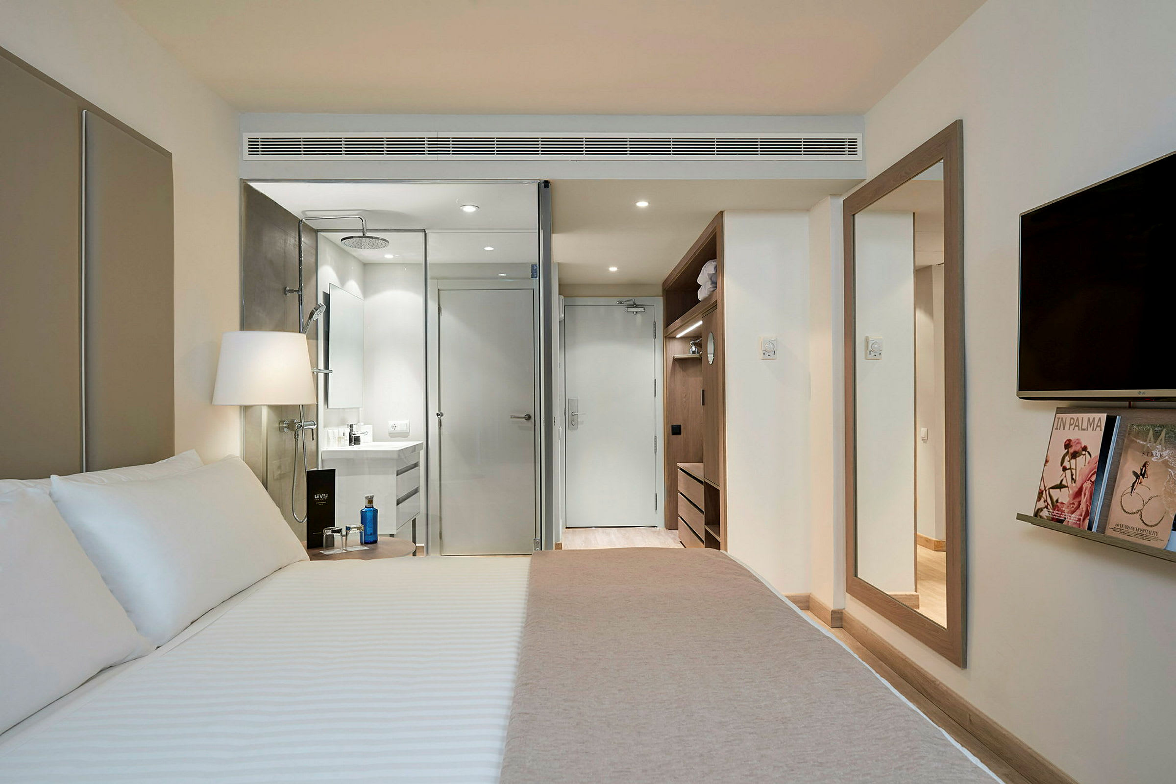 Et moderne hotellrom med en stor seng, et tilknyttet bad med glassvegg og en garderobe. (AI-generert tekst)