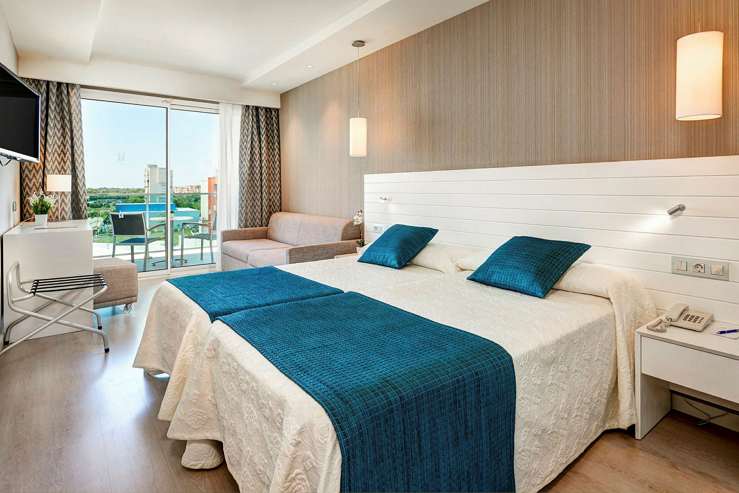 Hotellrom med to senger, en sofa og en glassbalkong. (AI-generert tekst)
