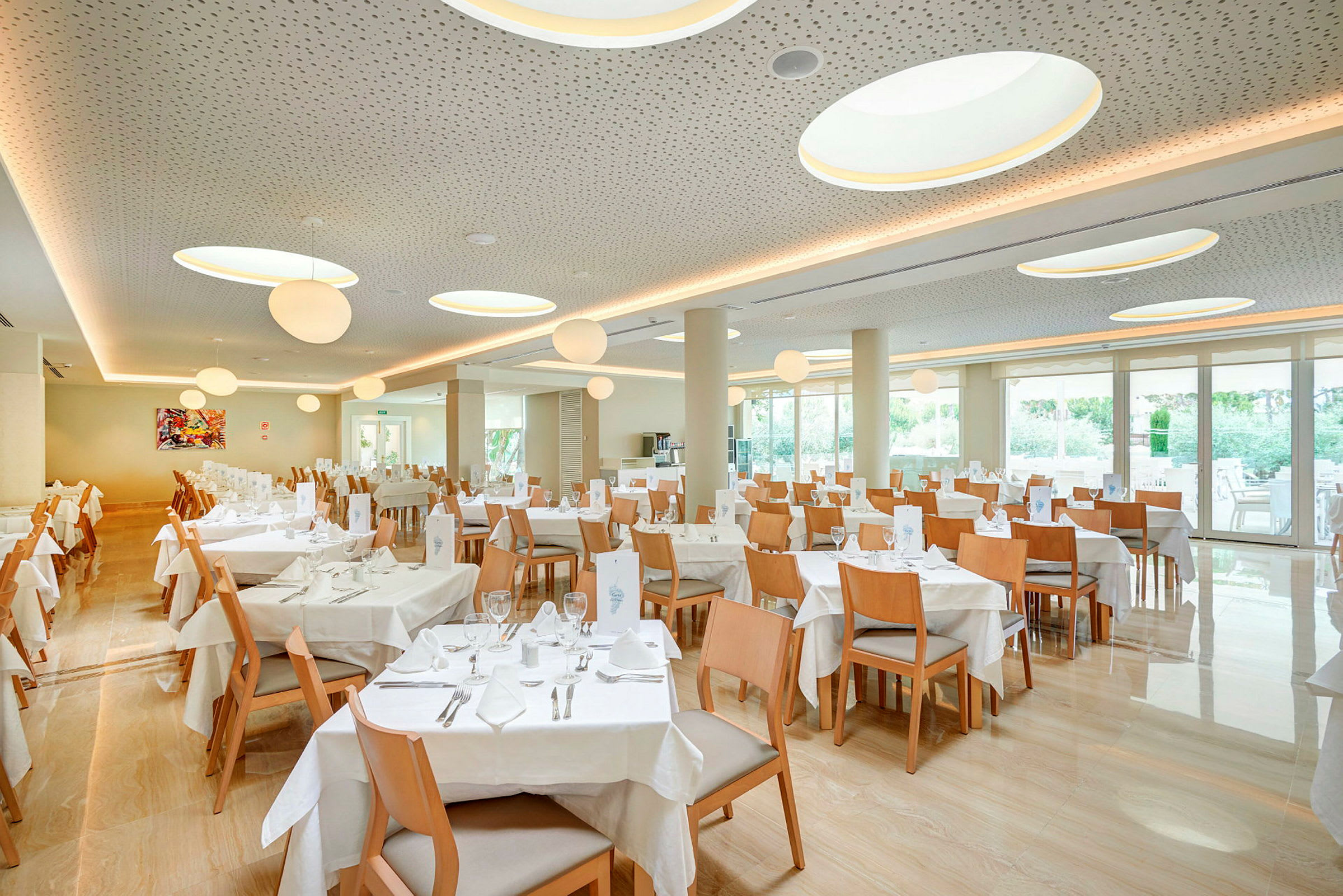 En restaurant med flere bord og trestoler, store vinduer og taklamper. (AI-generert tekst)