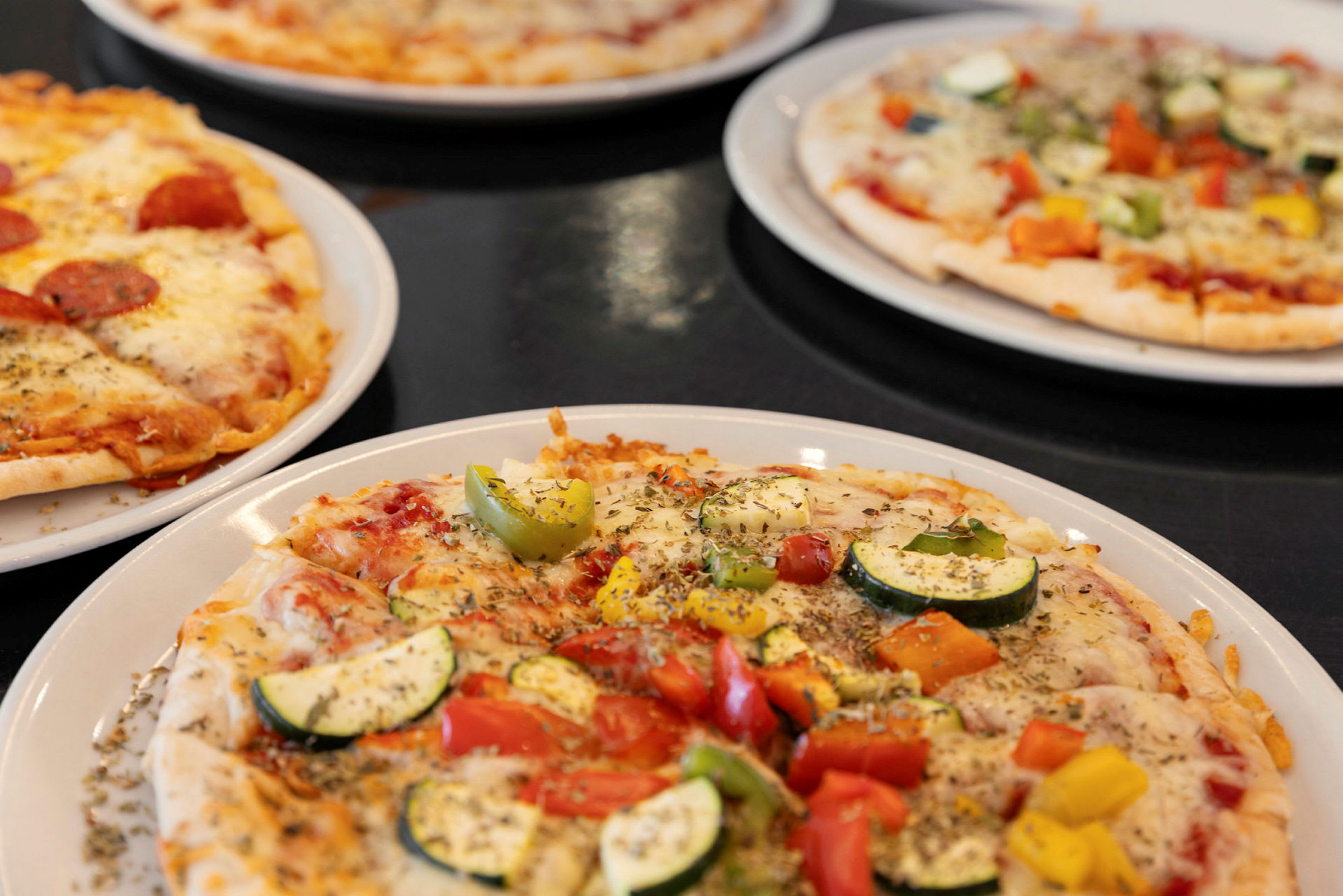 Fire pizzaer med forskjellige toppinger på tallerkener. (AI-generert tekst)