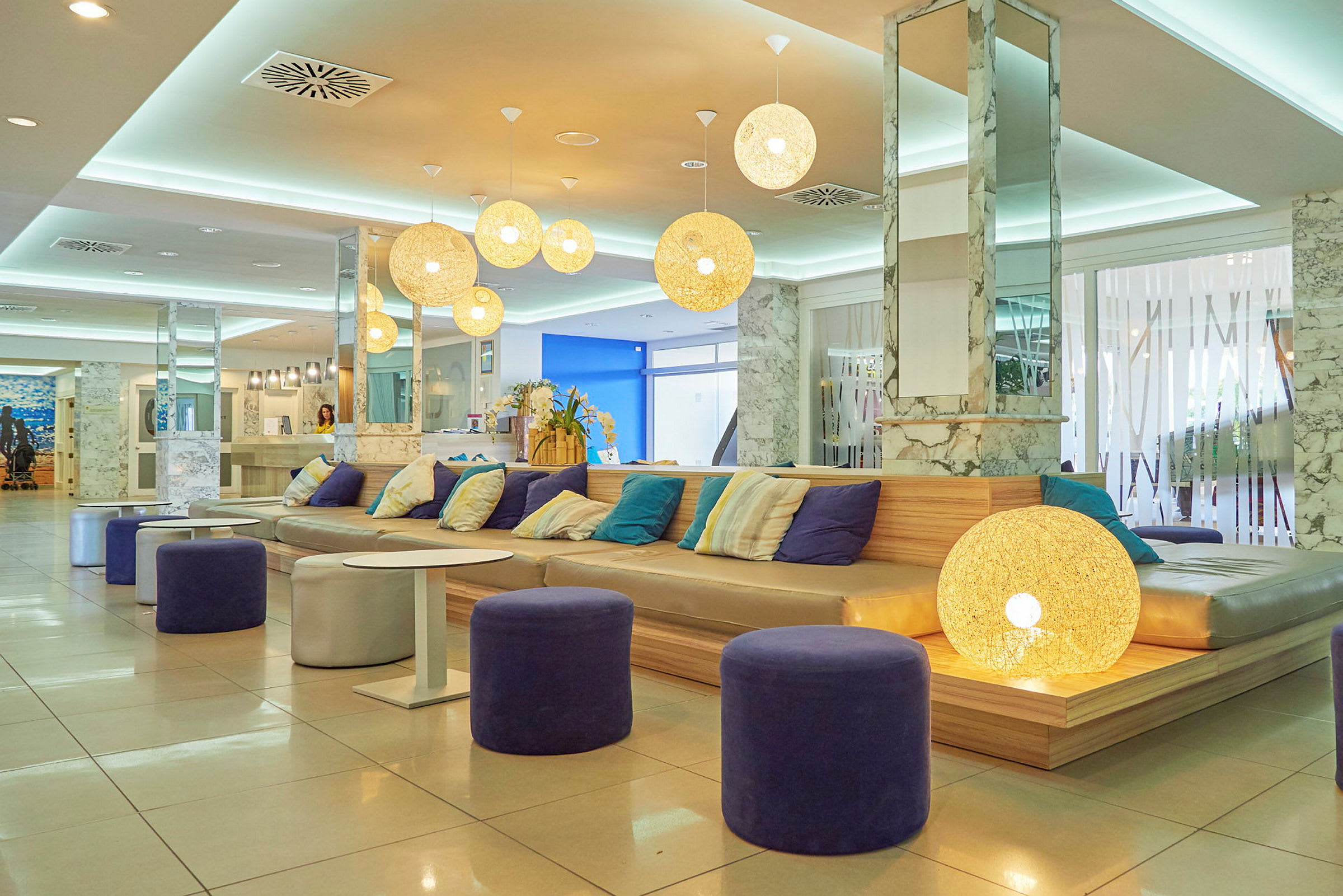 Hotellobby med sofaer og puter, bord og dekorative hengende lamper. (AI-generert tekst)
