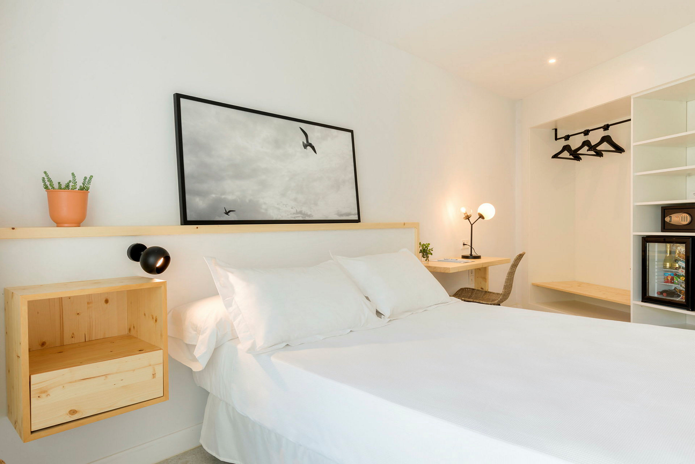 Et lyst hotellrom med en hvit seng, tremøbler og veggdekorasjon. (AI-generert tekst)
