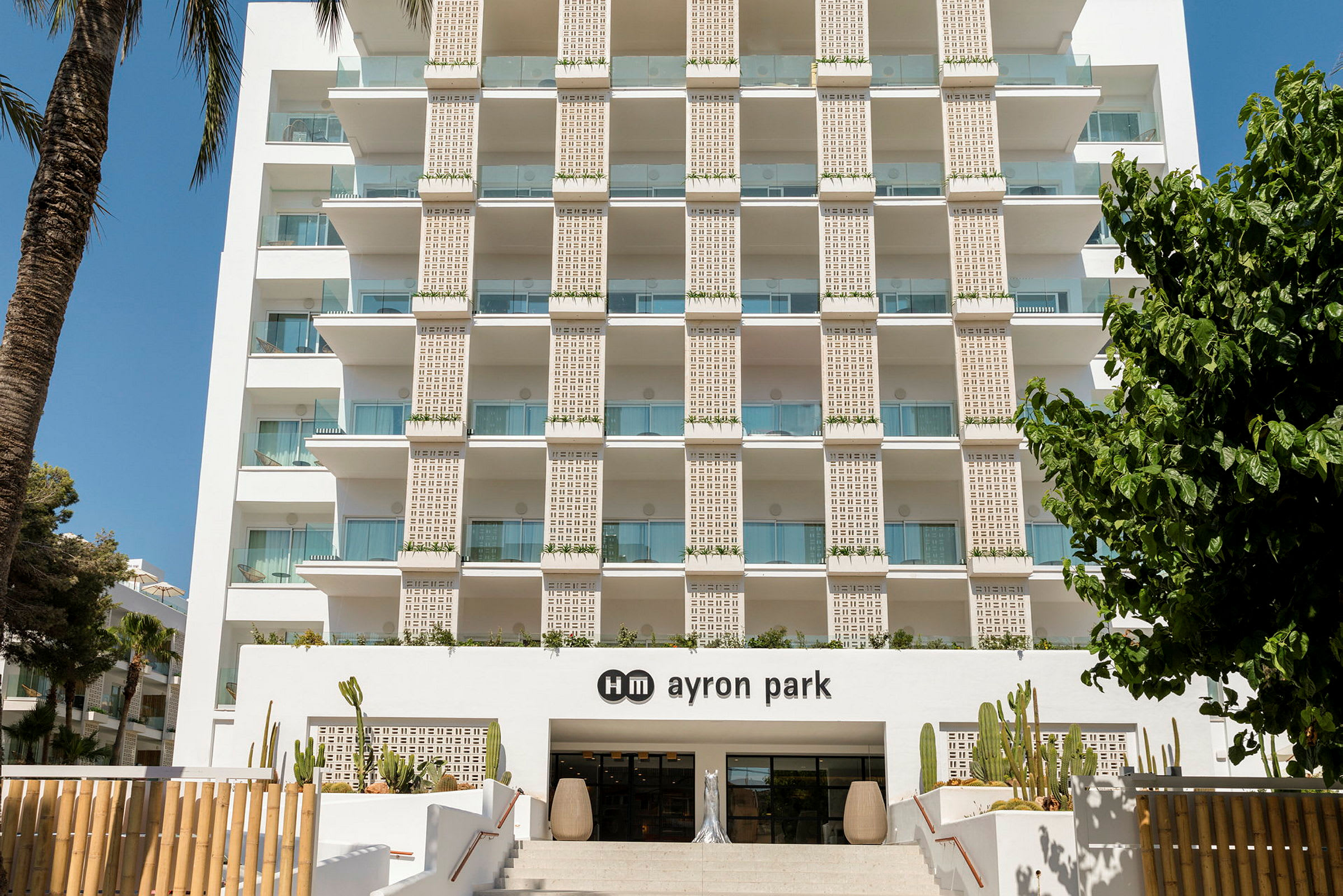 Hotellfasaden med balkonger og inngangen til hm ayron park, dekorert med kaktus. (AI-generert tekst)