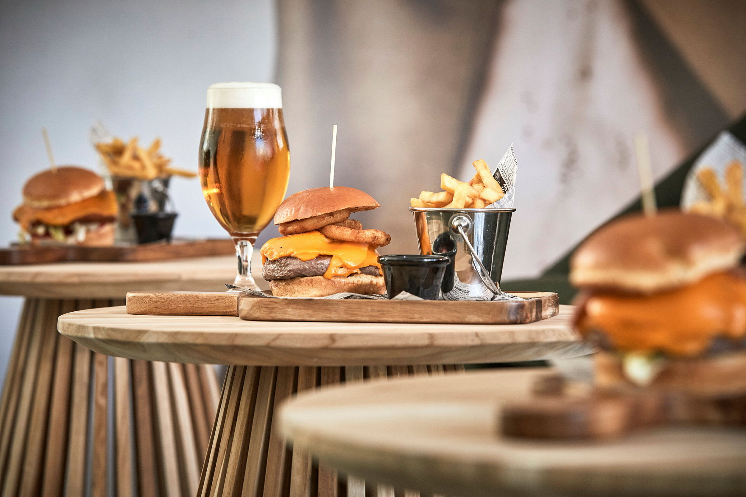 Tallerkener med hamburgere, pommes frites i metallbøtte og glass med øl på trebord. (AI-generert tekst)
