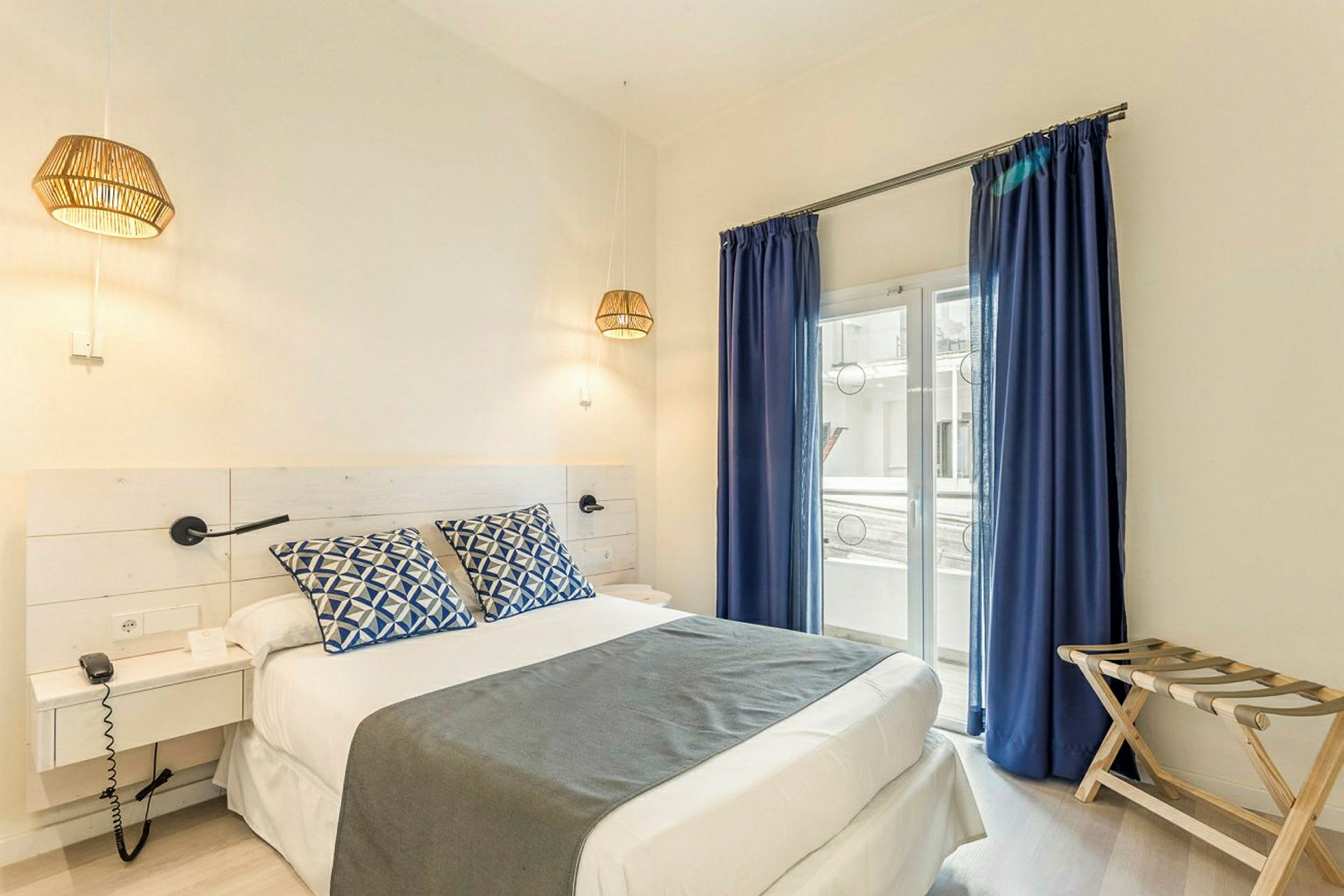 Et hotellrom med en dobbeltseng, blå gardiner og vindu mot en balkong. (AI-generert tekst)