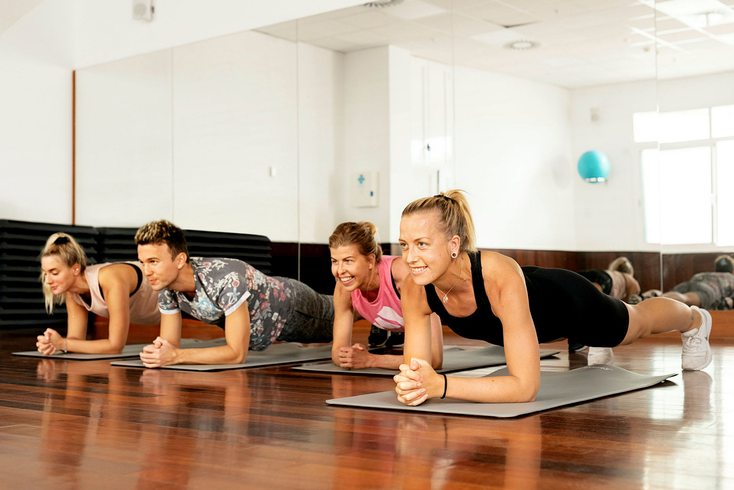 Personer utfører plankeøvelser på yogamatter i et lyst rom med speilvegg. (AI-generert tekst)