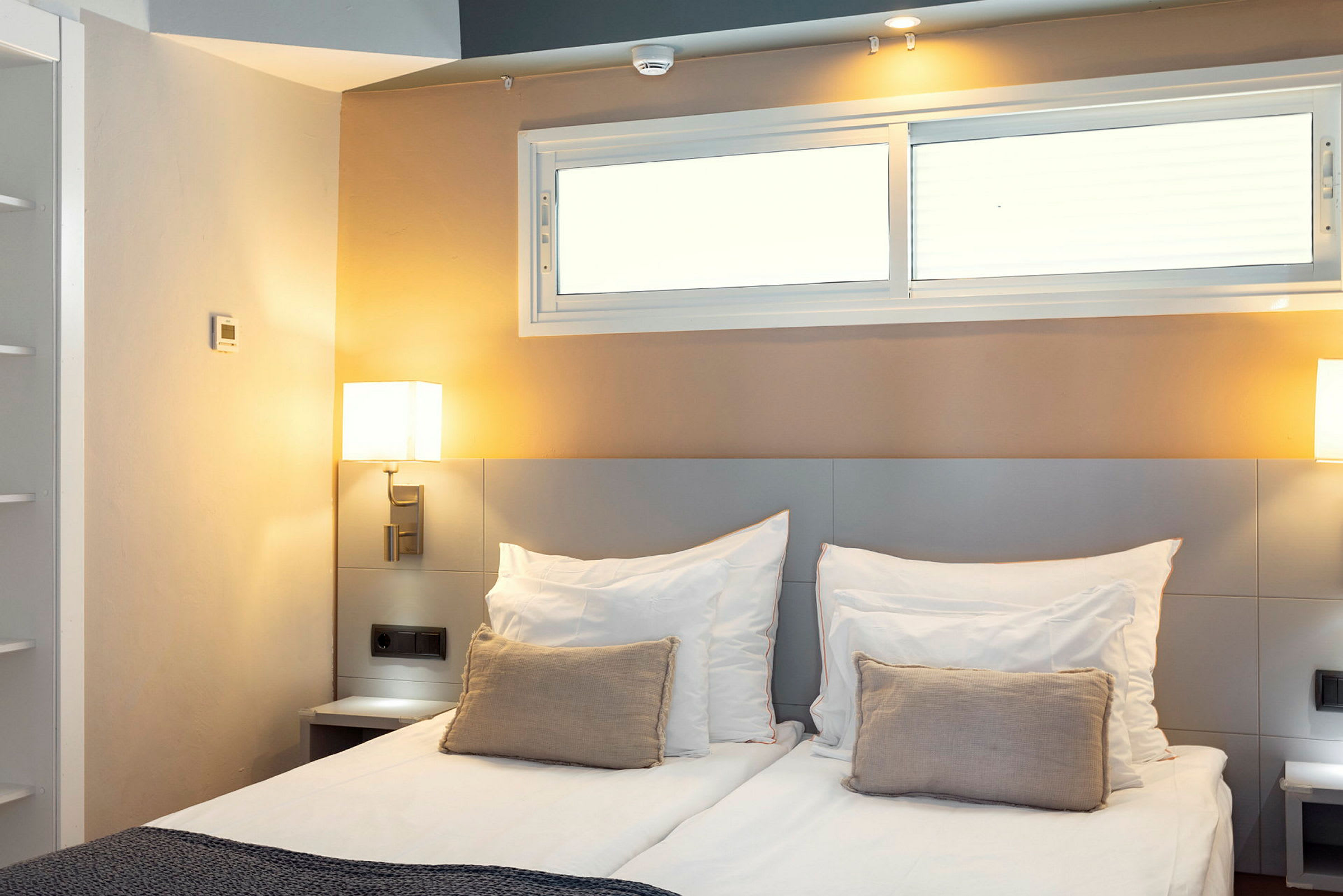 Et hotellrom med en dobbeltseng, dekorativ pute og senge lamper ved siden av. (AI-generert tekst)