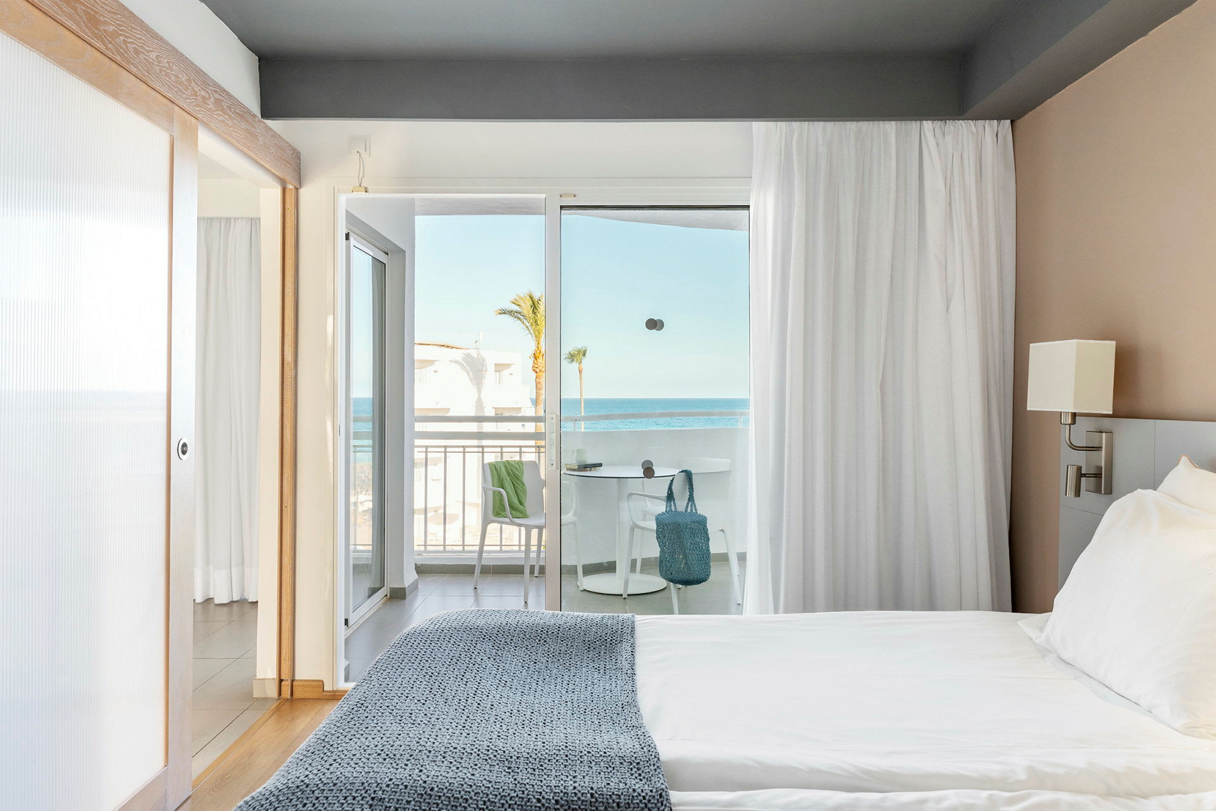 Hotellrom med seng nær et lysinnslipp mot en balkong med havutsikt. (AI-generert tekst)