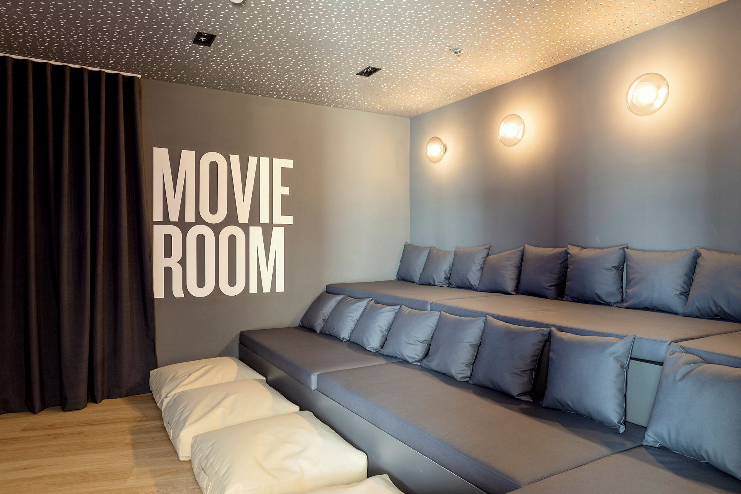 Bilde av et kinorom med opphøyde sitteplasser med puter og teksten 'Movie Room' på veggen. (AI-generert tekst)