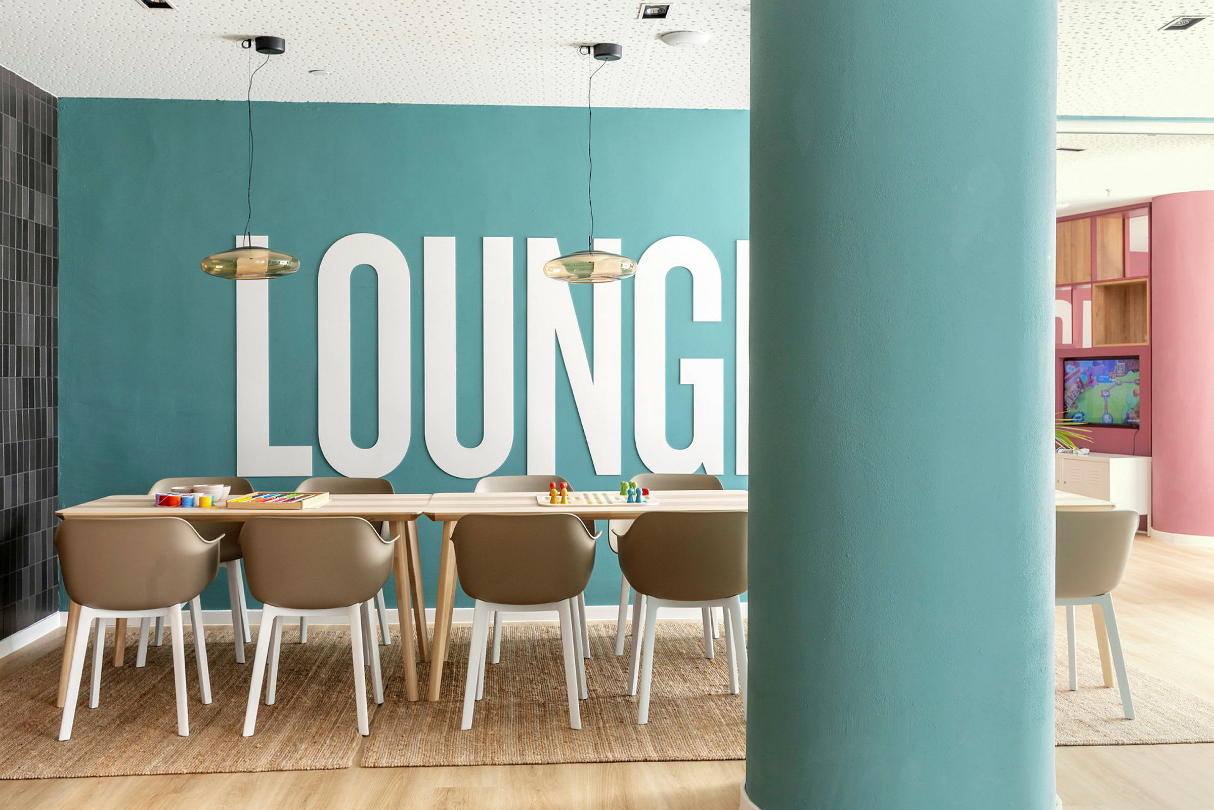 Et bilde av et rom med et teppe, stoler og et bord foran en blå vegg med teksten 'LOUNGE'. (AI-generert tekst)