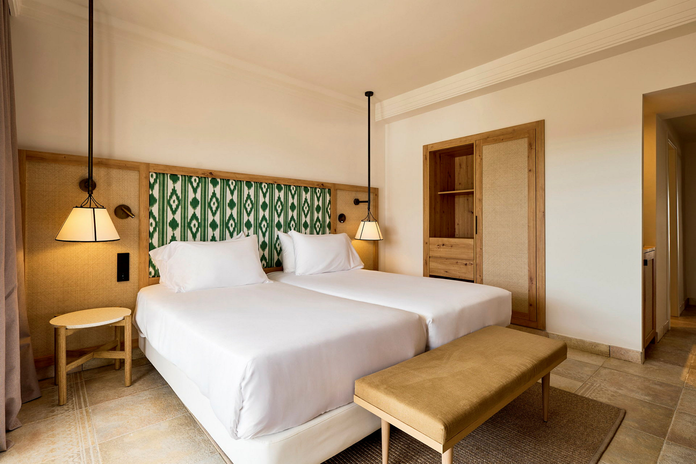 Et hotellrom med to enkeltsenger, en benk og innebygd garderobe. (AI-generert tekst)
