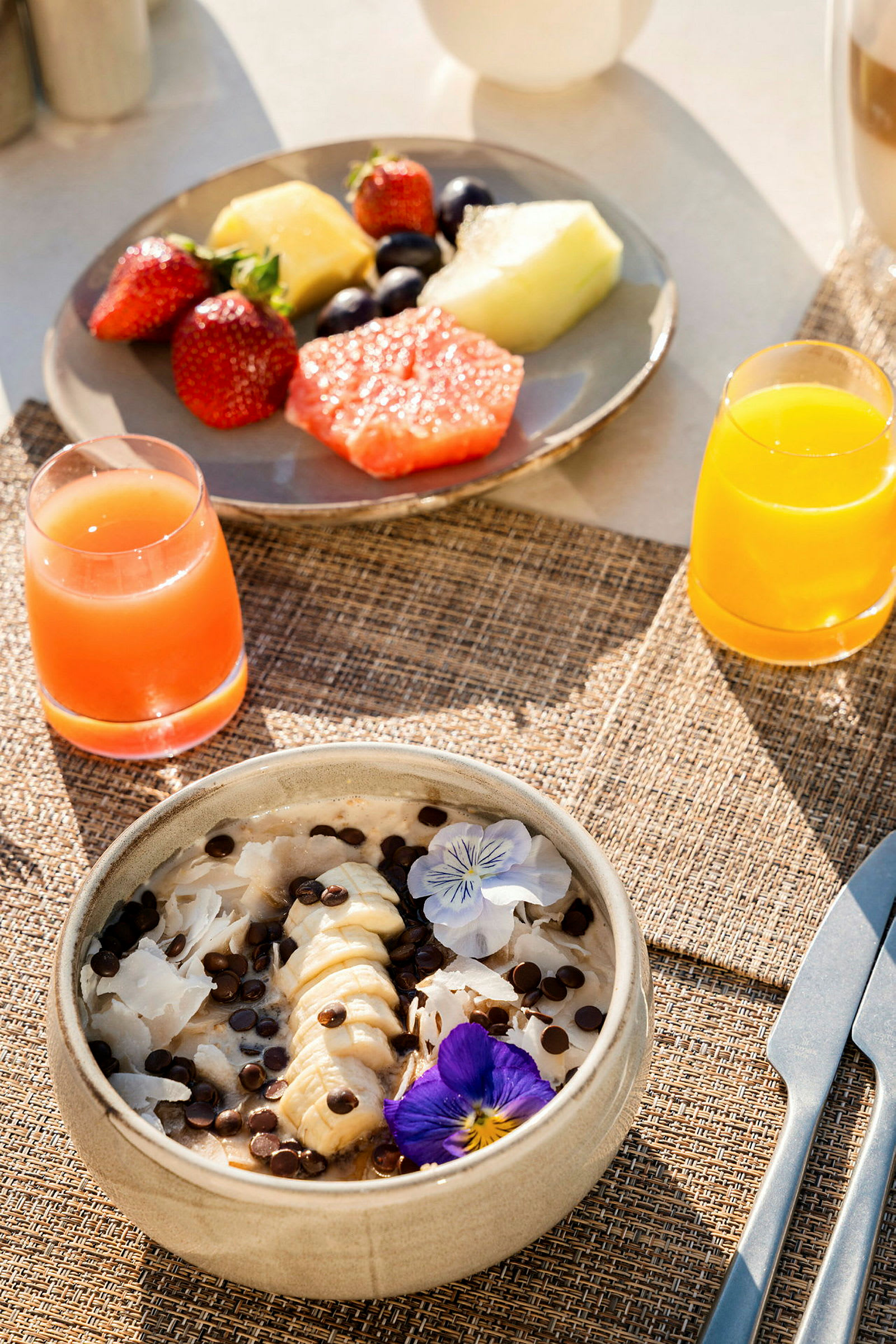 Frokostbord med fersk frukt, en bolle med bananskiver og sjokoladebiter, samt juice. (AI-generert tekst)