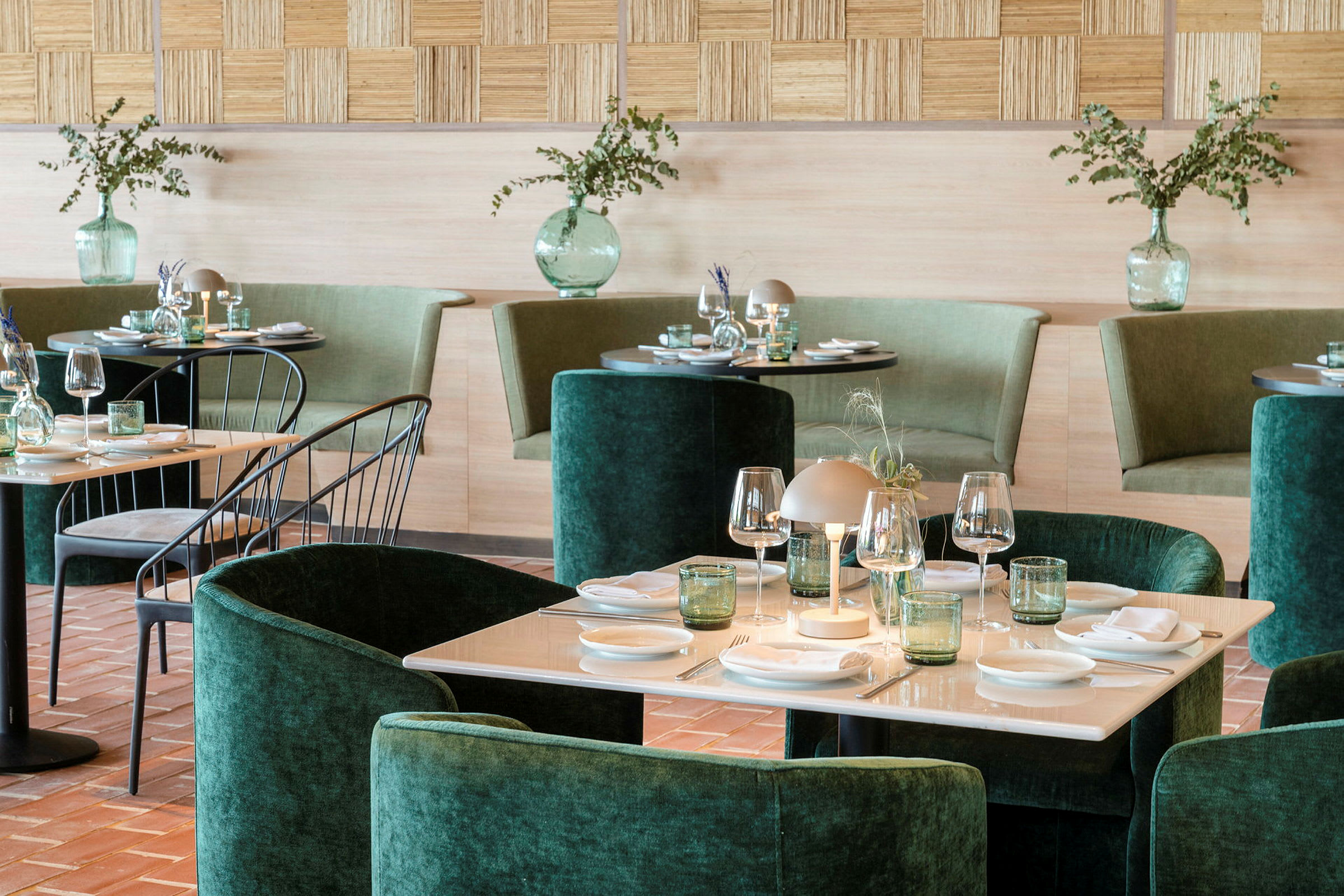 Et elegant innredet restaurantområde med grønn stopping, dekkede bord og dekorative vaser med planter. (AI-generert tekst)