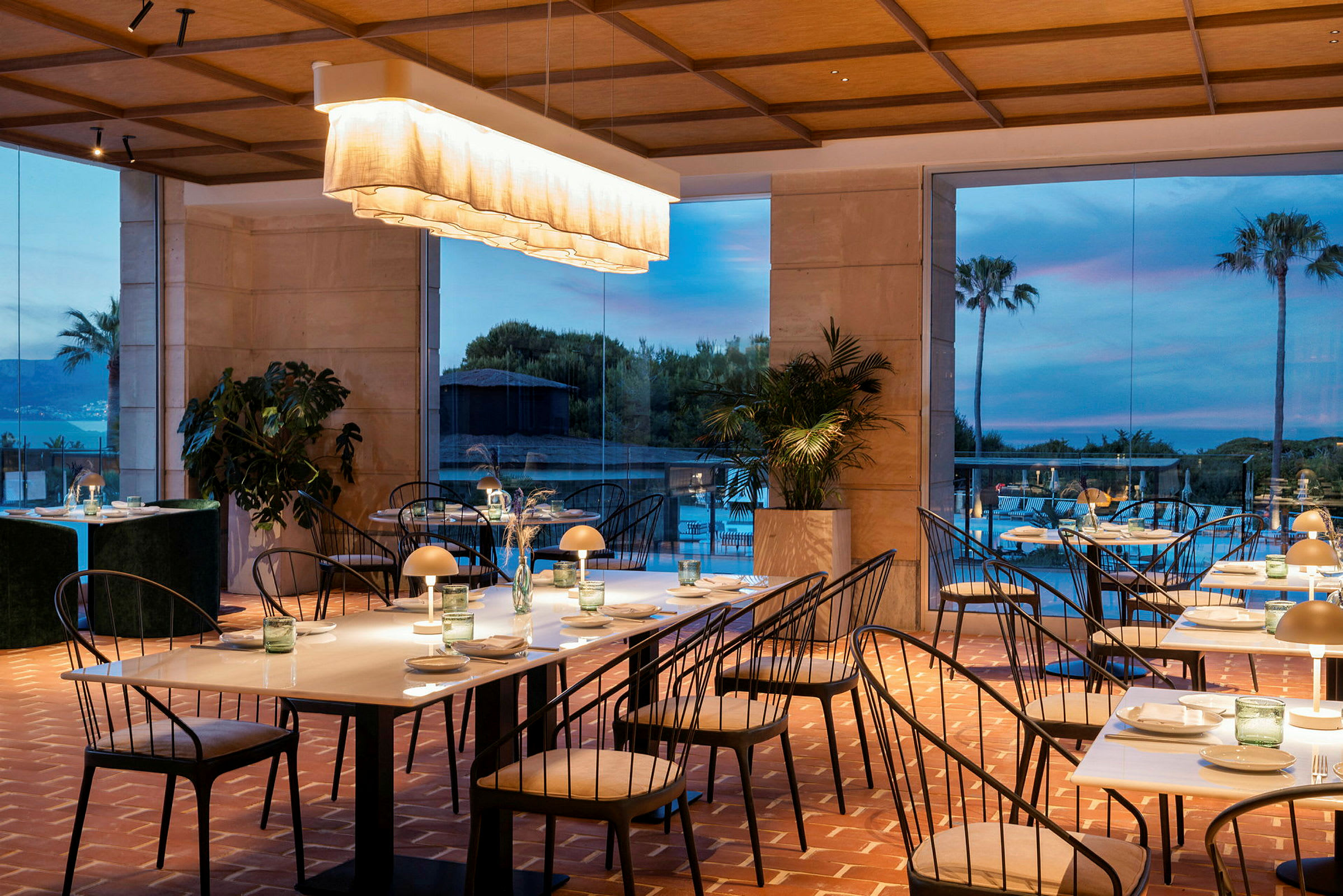 En elegant innredet restaurant med bord og stoler samt en lys innredning. I bakgrunnen vises store vinduer med naturskjønn utsikt. (AI-generert tekst)