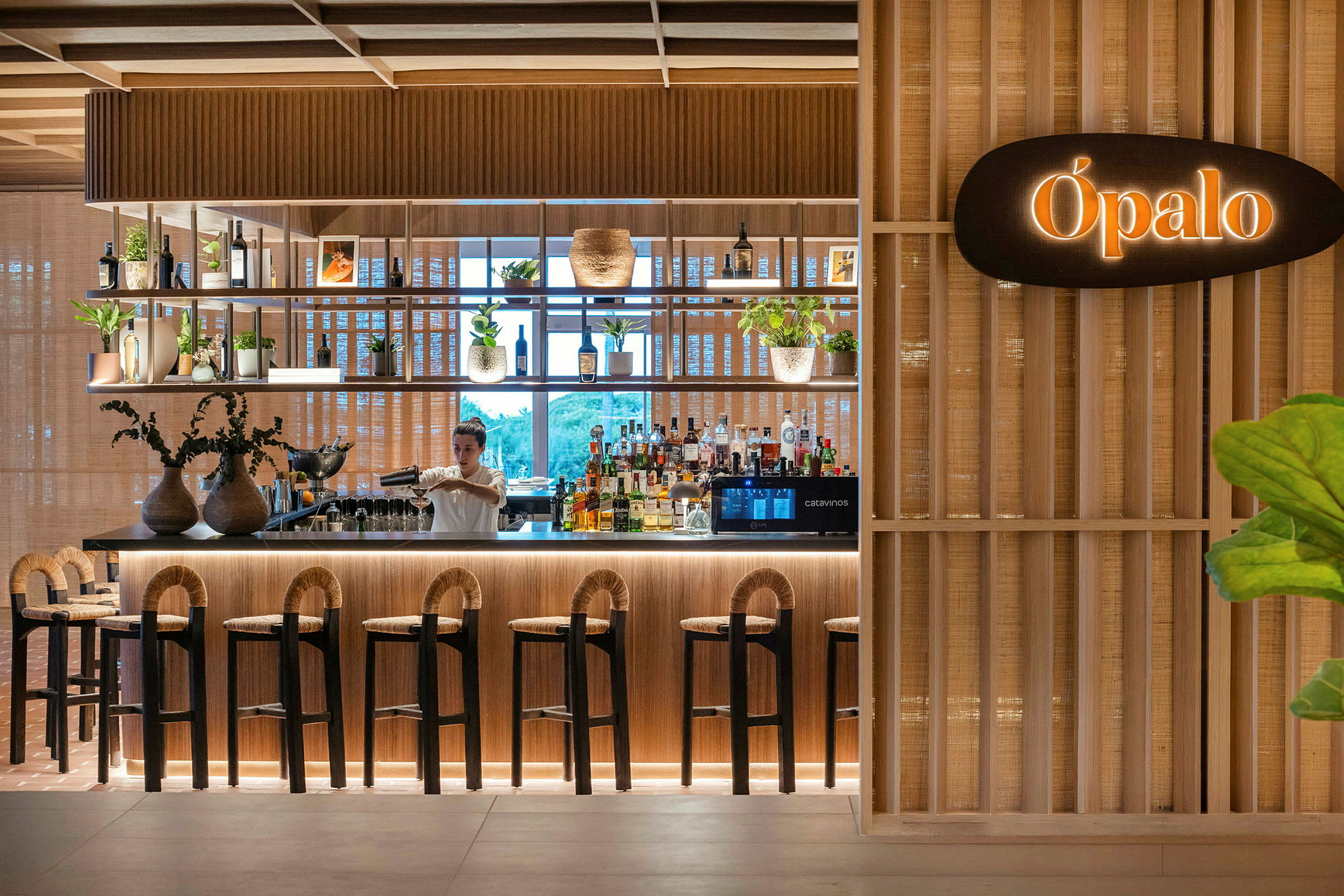 En elegant bar med tredetaljer og planter, hvor en bartender lager en drink. (AI-generert tekst)