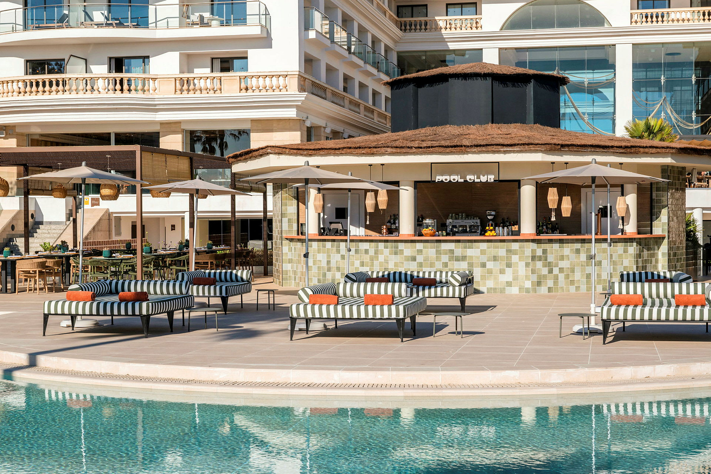 Et basseng med solsenger, parasoller og en bar med skilt "Pool Club" i bakgrunnen. (AI-generert tekst)
