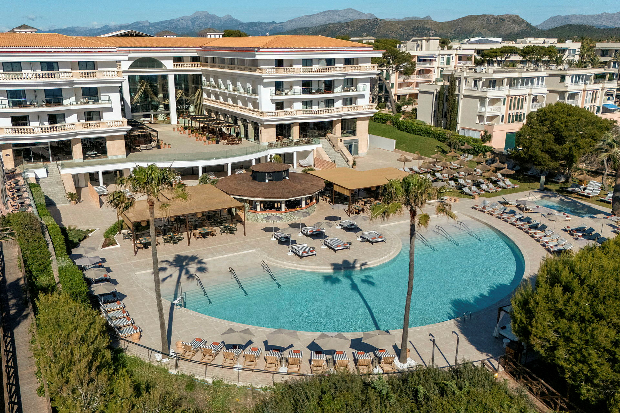 Hotell med basseng- og terrasseområde omgitt av solsenger, parasoller og grøntområder. (AI-generert tekst)