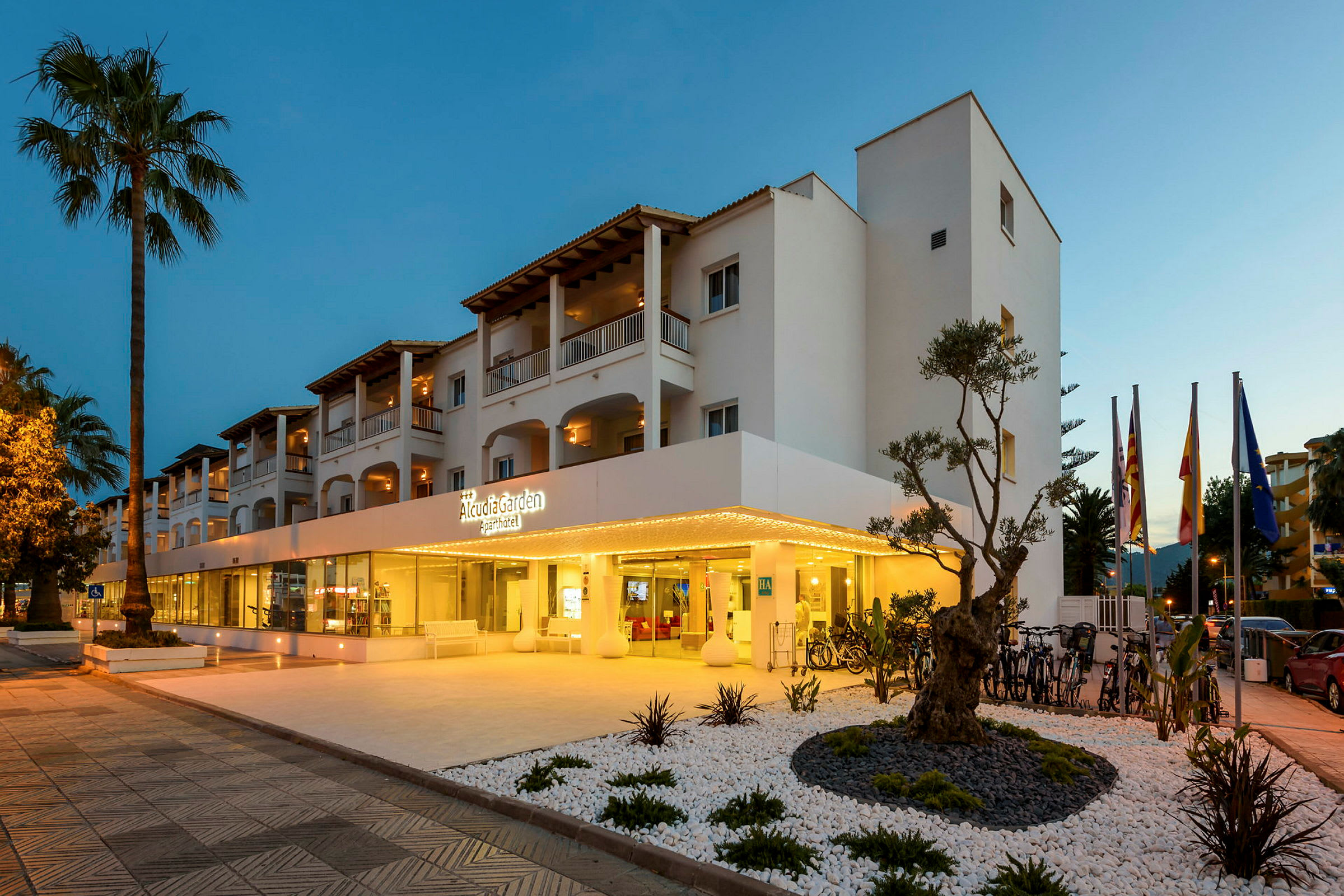 Bilde av hotellet Alcudia Garden Aparthotel, med opplyst inngang og omkringliggende hage. (AI-generert tekst)
