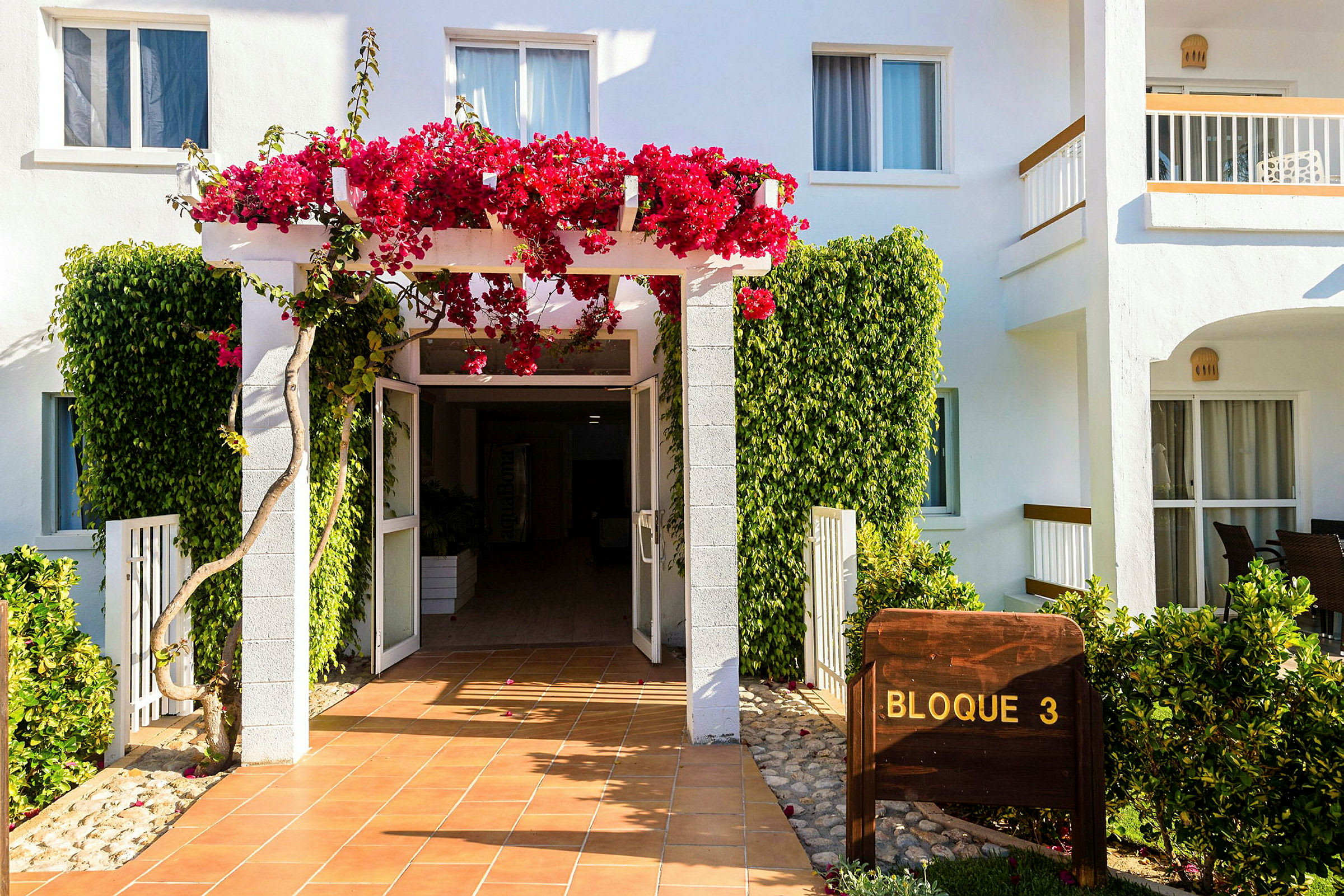 Inngangen til en bygning med hvite vegger og blomster som klatrer på en pergola. (AI-generert tekst)