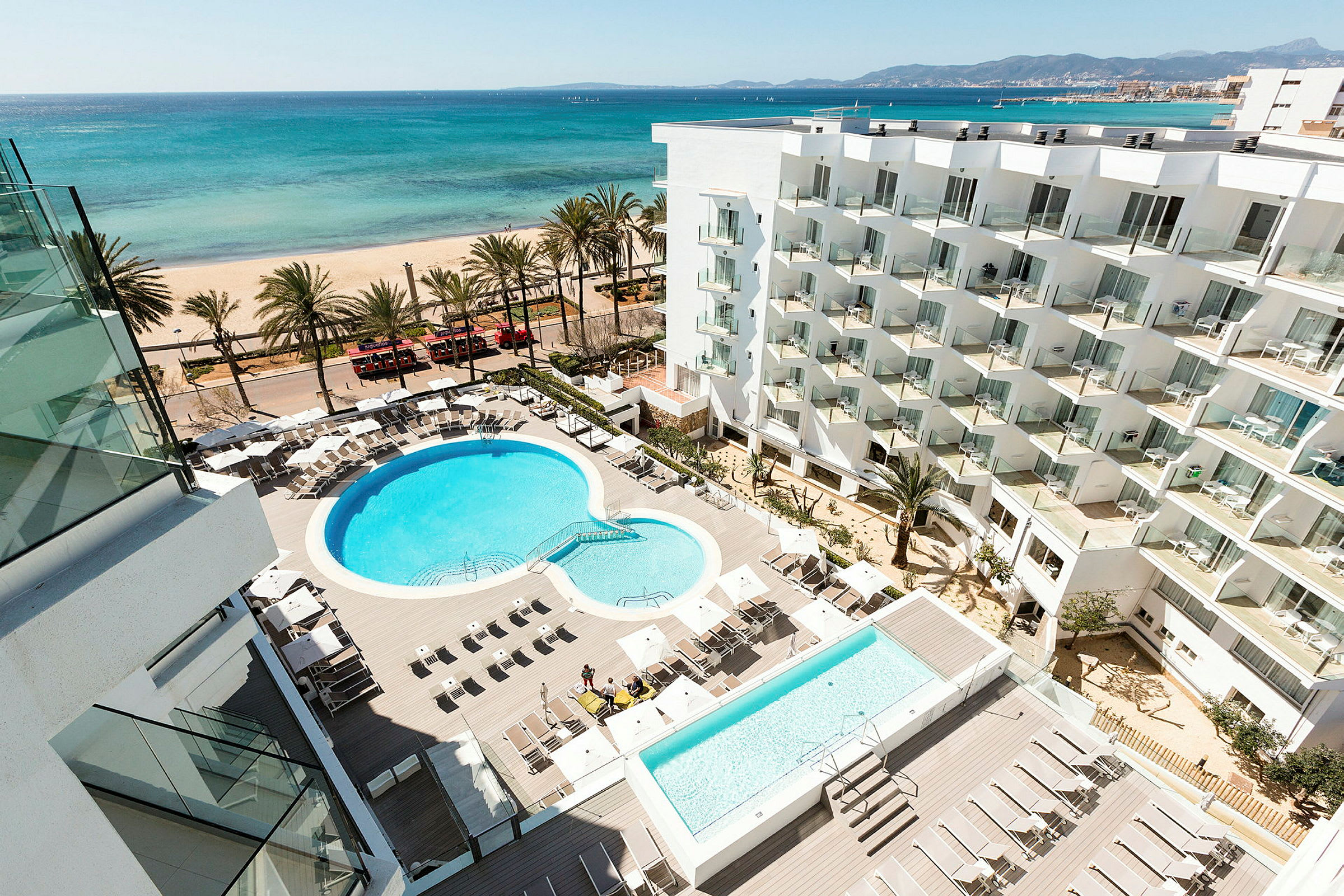 Hotellområde med basseng og solsenger, strand og hav i bakgrunnen. (AI-generert tekst)
