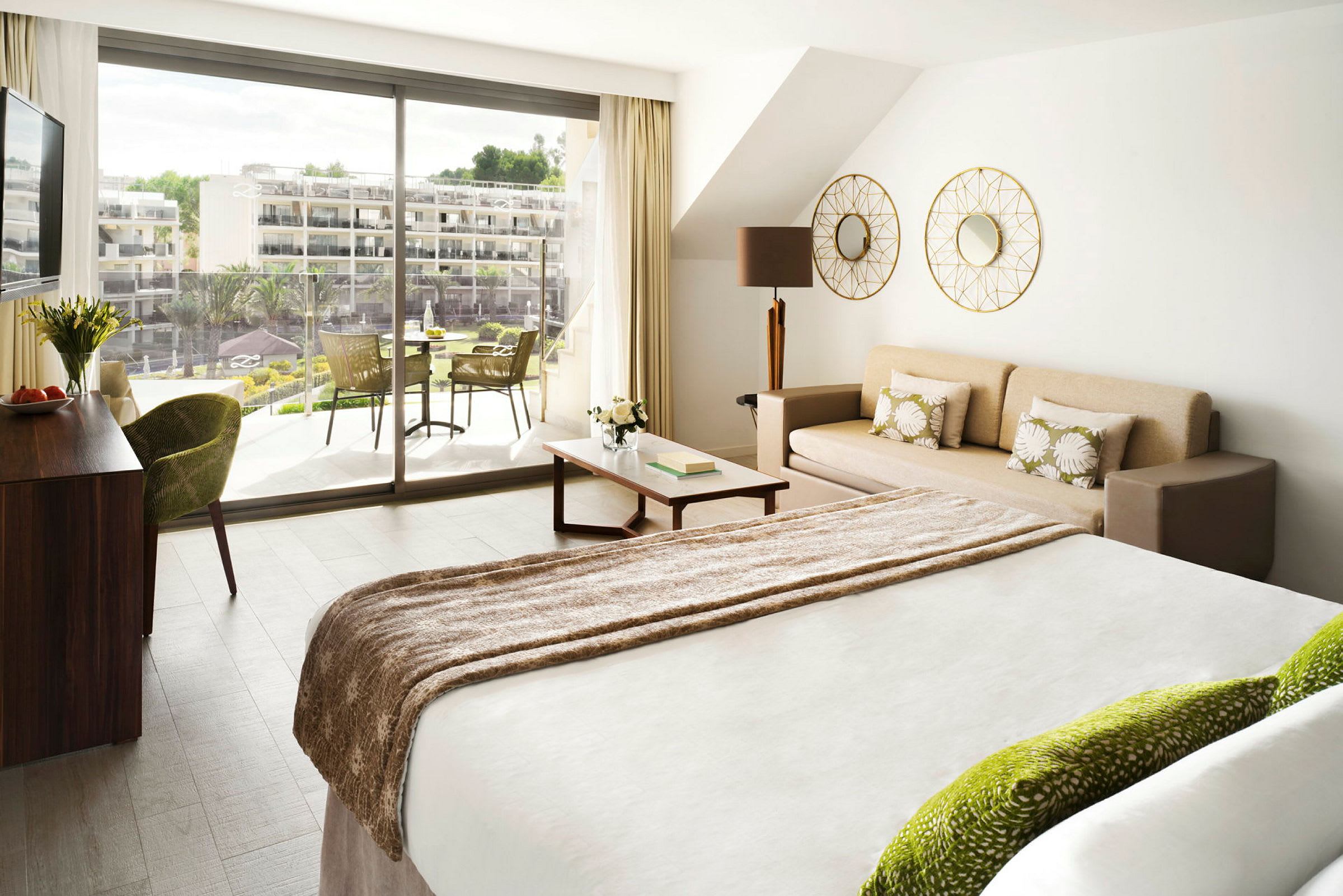 Et lyst hotellrom med en seng, en sofa og en balkong utenfor. (AI-generert tekst)