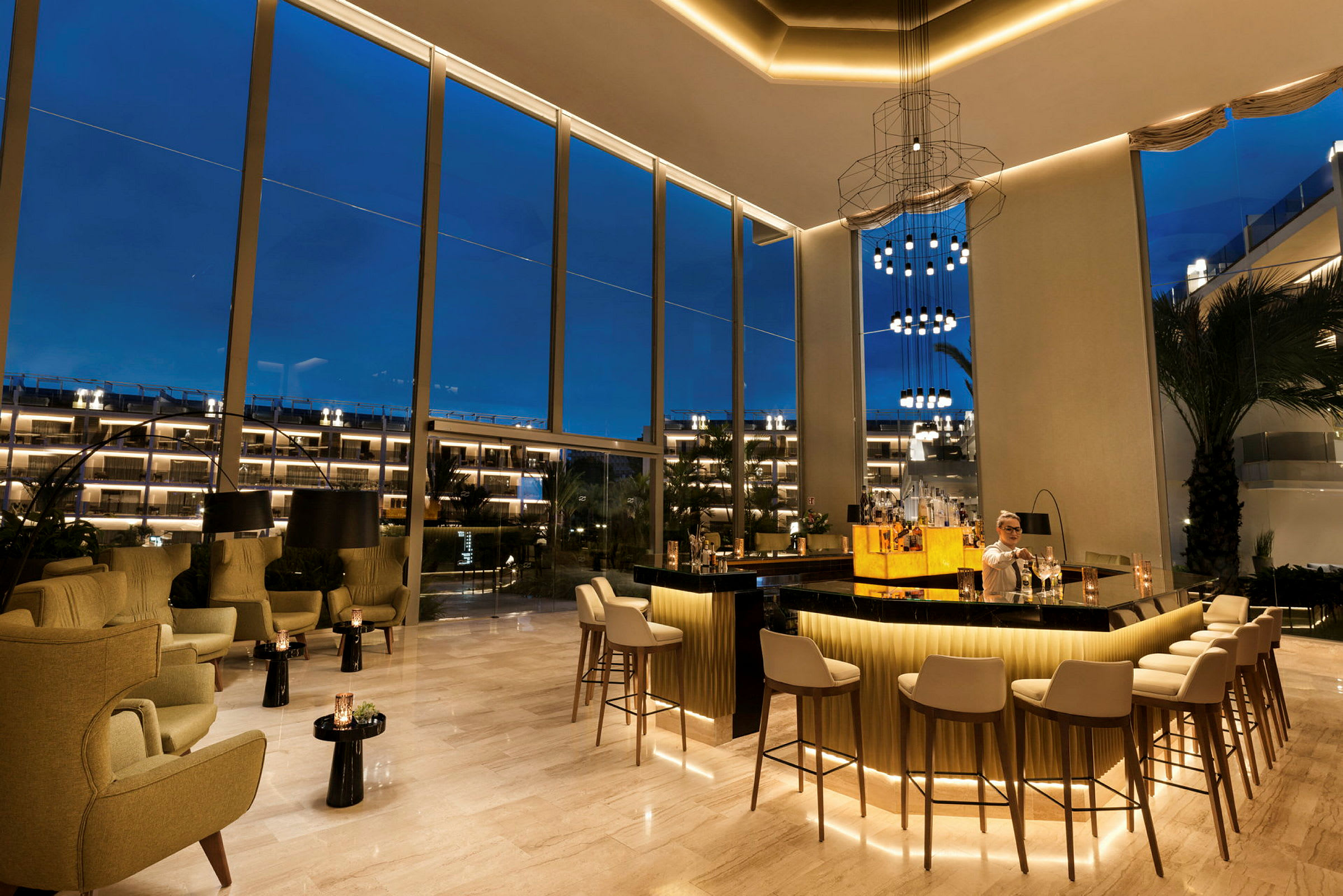 En elegant bar med sitteplasser og høye vinduer som vender mot utendørs kveldsbelysning. (AI-generert tekst)
