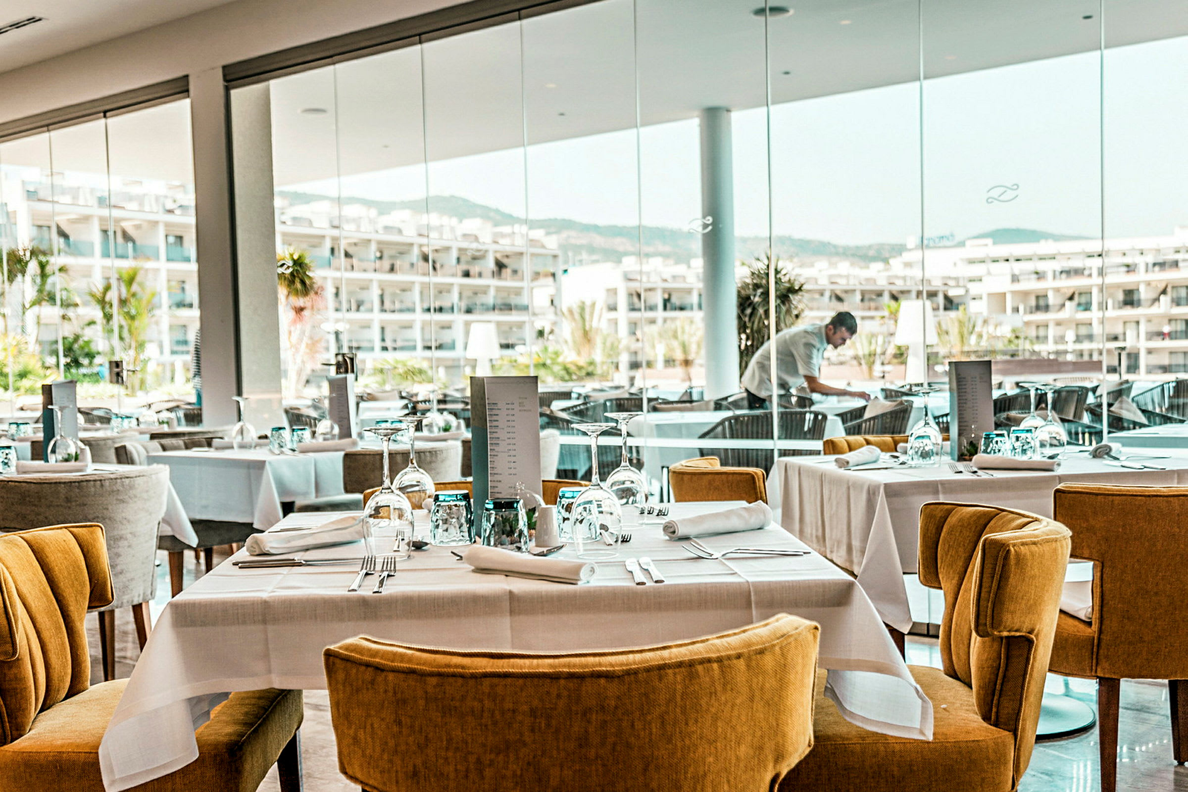 En moderne restaurant med dekkede bord og stoler samt vinduer med utsikt over et hotellområde. (AI-generert tekst)