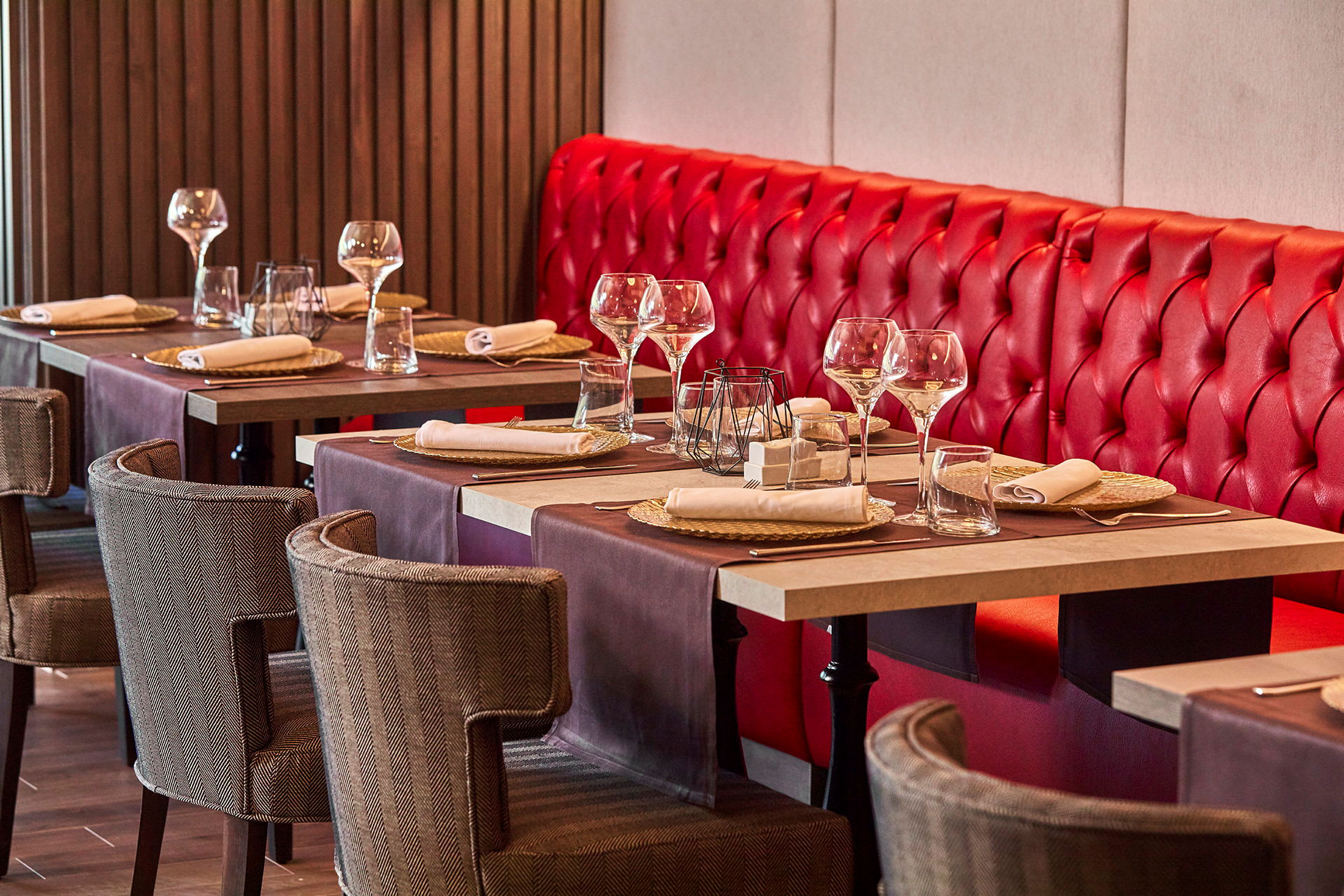 Et restaurantbord med rød benkesete og dekkede bord med glass og servietter. (AI-generert tekst)
