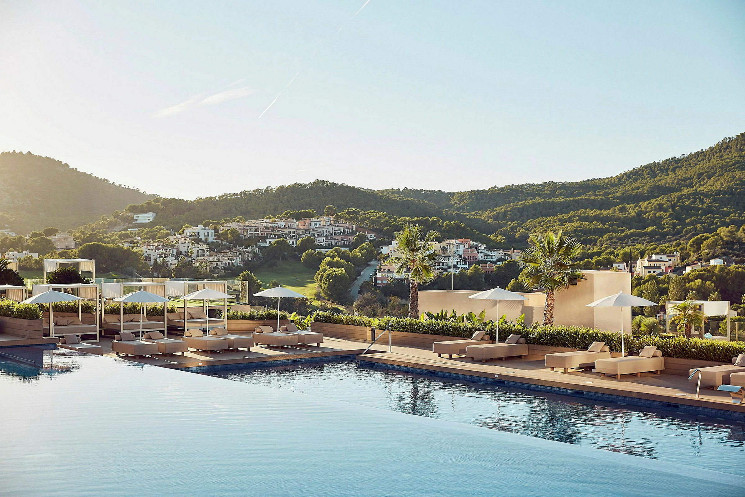 En utsikt fra et hotellområde med et basseng omgitt av solsenger, parasoller og et frodig landskap i bakgrunnen. (AI-generert tekst)