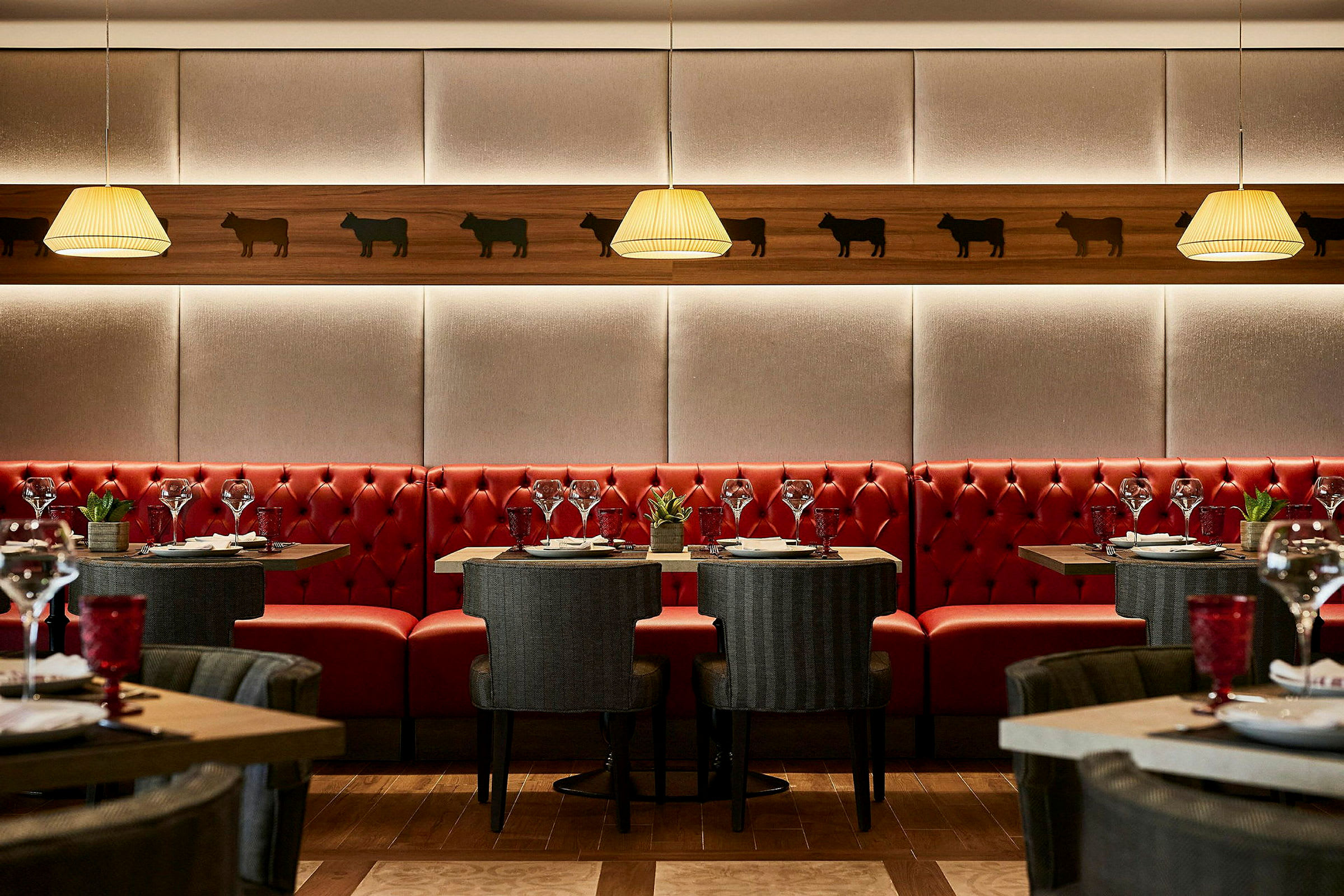 Restaurantinteriør med røde sofaer, elegante bord og stoler, samt veggdekorasjoner. (AI-generert tekst)