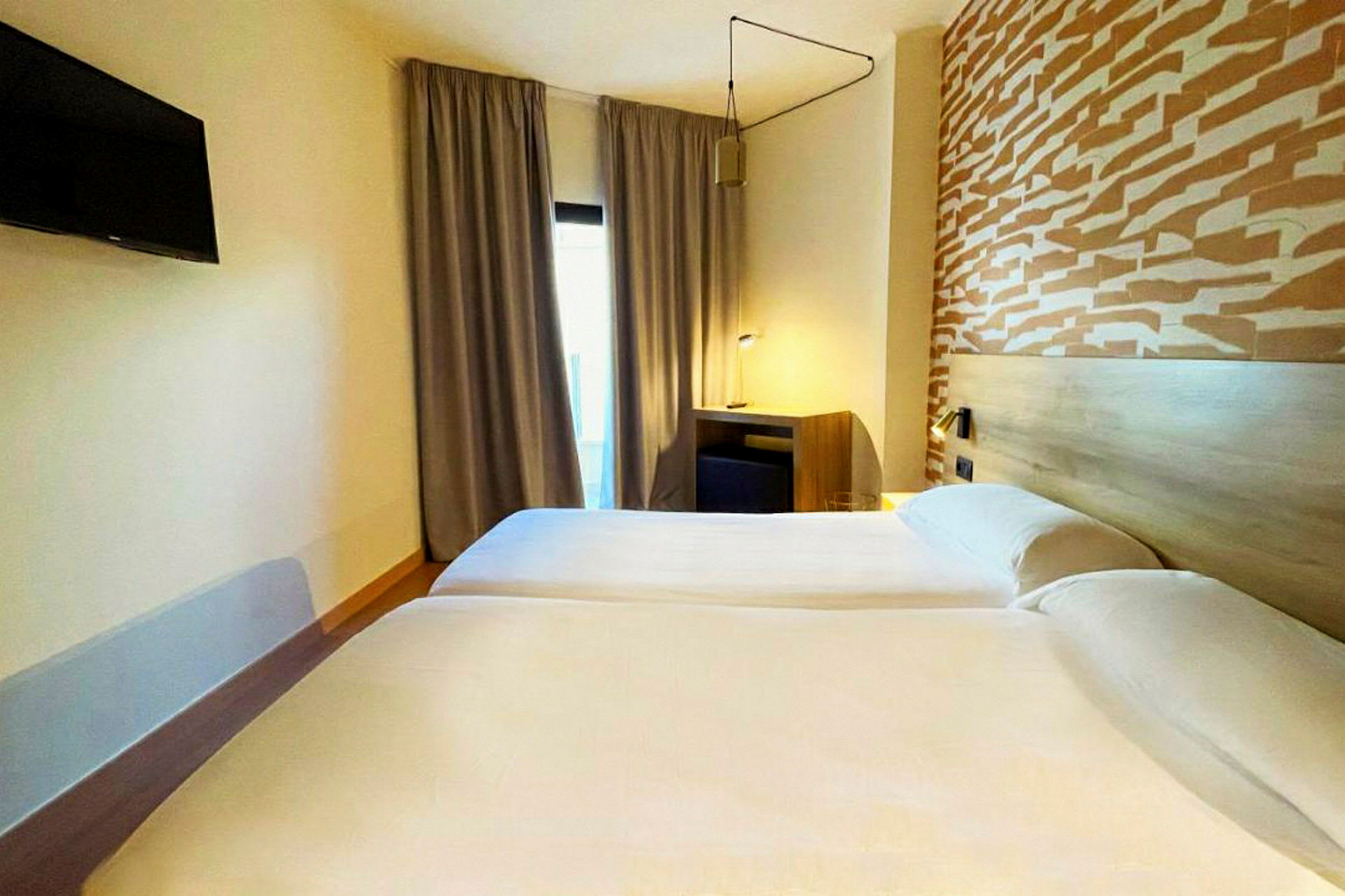 To enkeltsenger på et hotellrom med et mønstret hodegjerde og en TV på veggen. (AI-generert tekst)