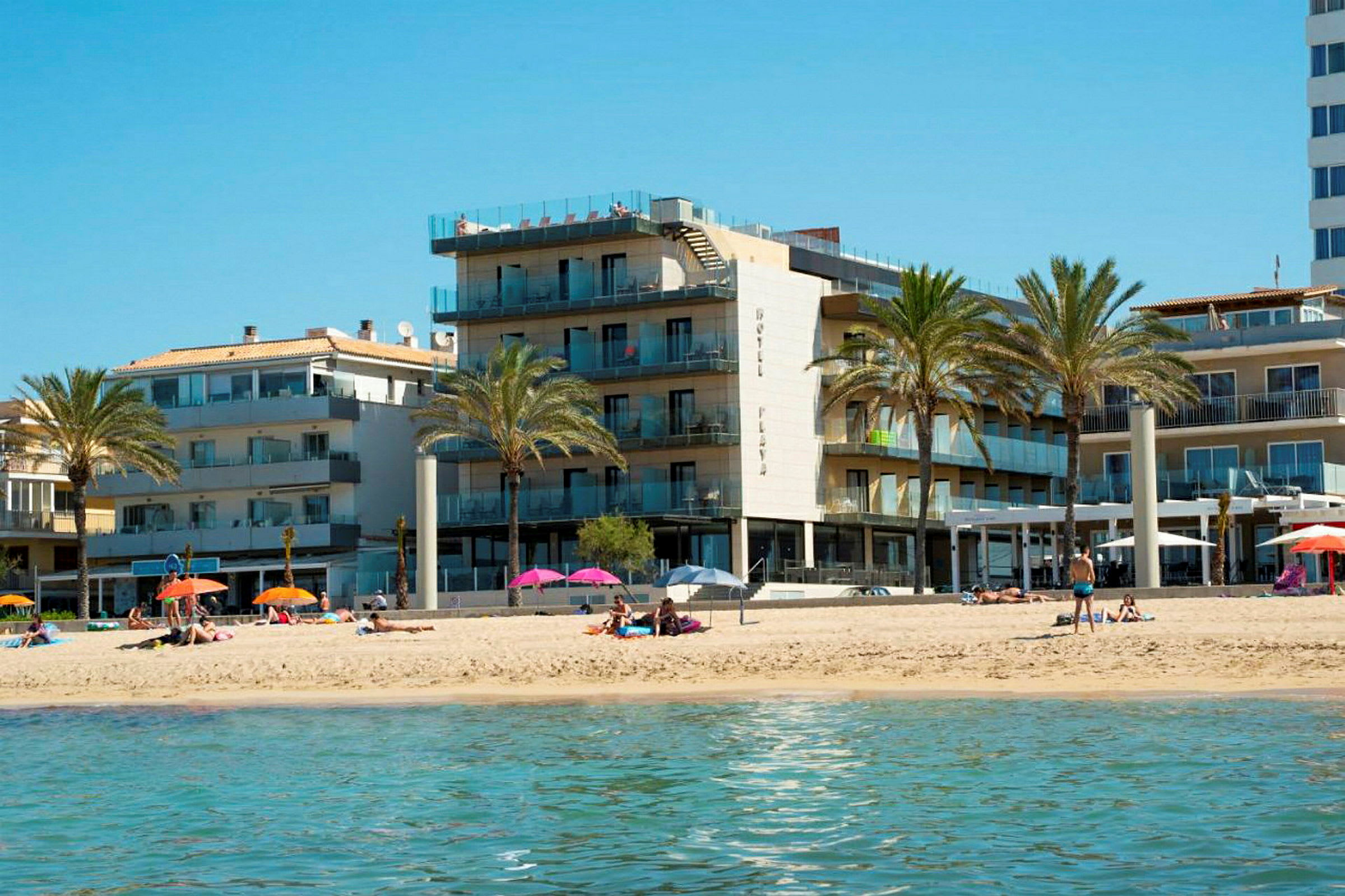En sandstrand foran et hotell med palmer. (AI-generert tekst)