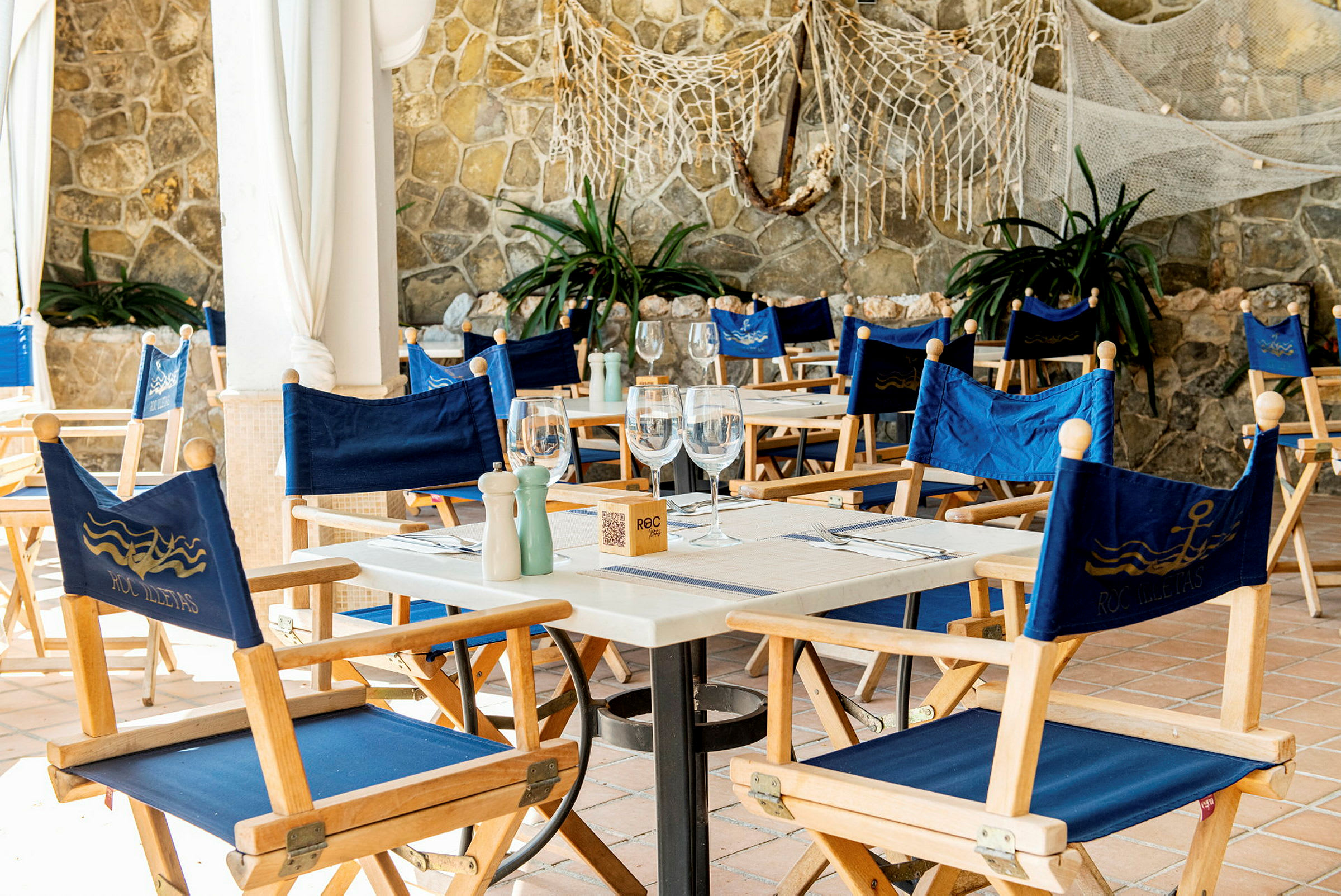 Et bord med blå stoler på en restaurant med steinmur i bakgrunnen. (AI-generert tekst)