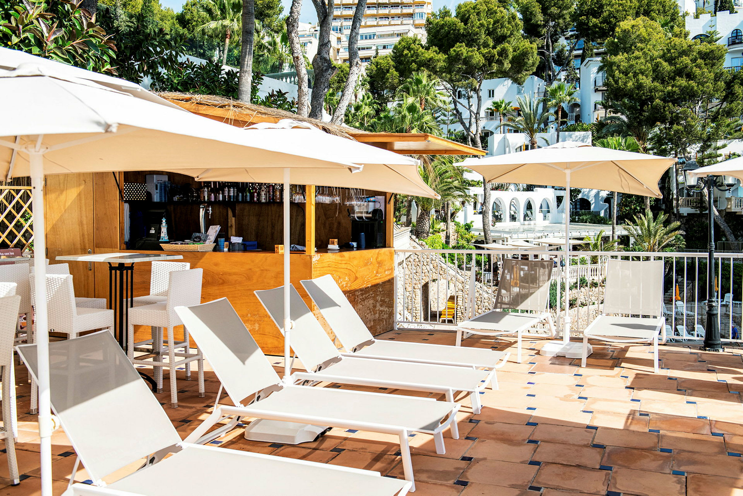 Solstoler og parasoller på en terrasse ved en bar, med utsikt over trær og bygninger. (AI-generert tekst)