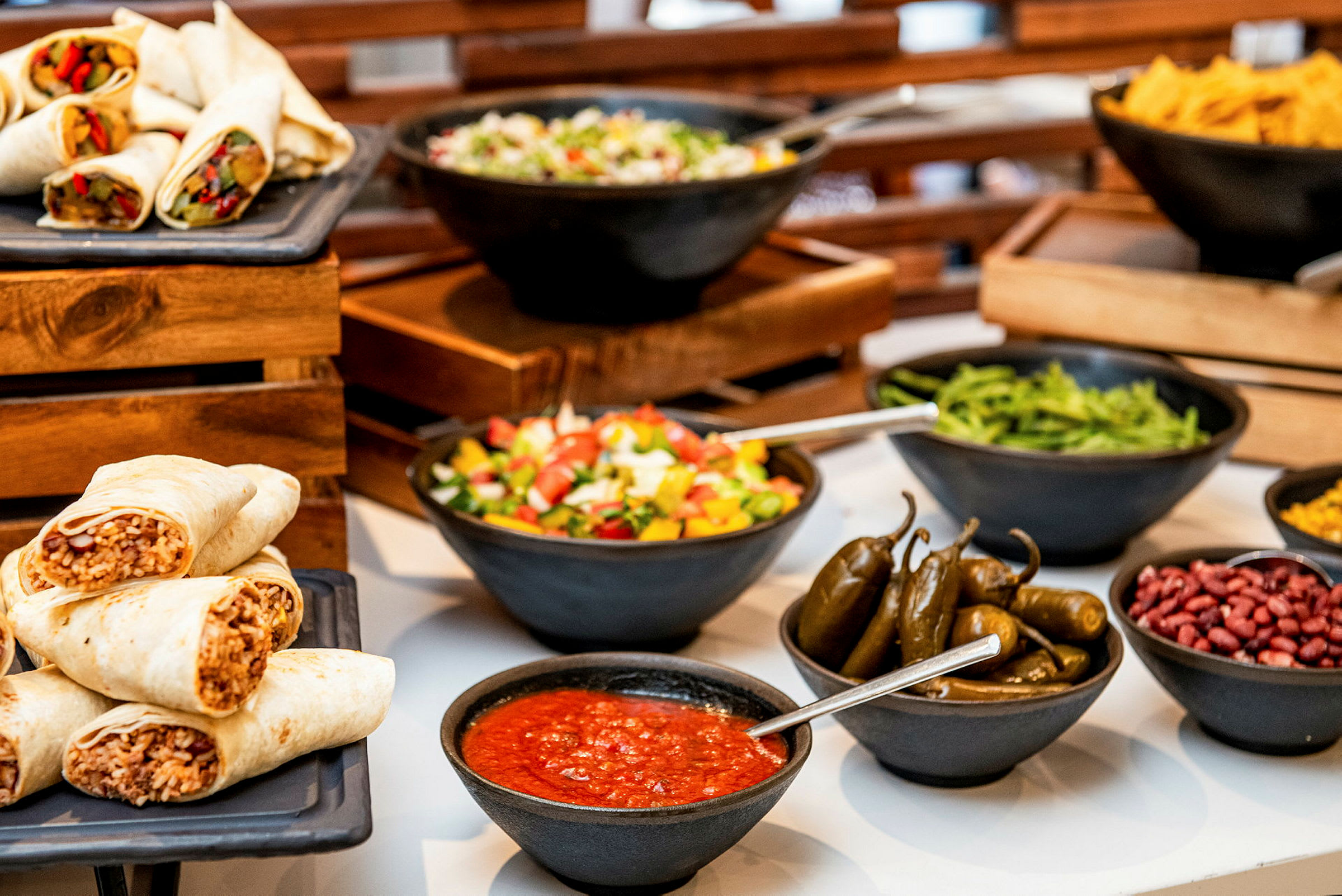 Bilde av en buffé med burritos, salat, jalapeños, saus og andre tilbehør. (AI-generert tekst)