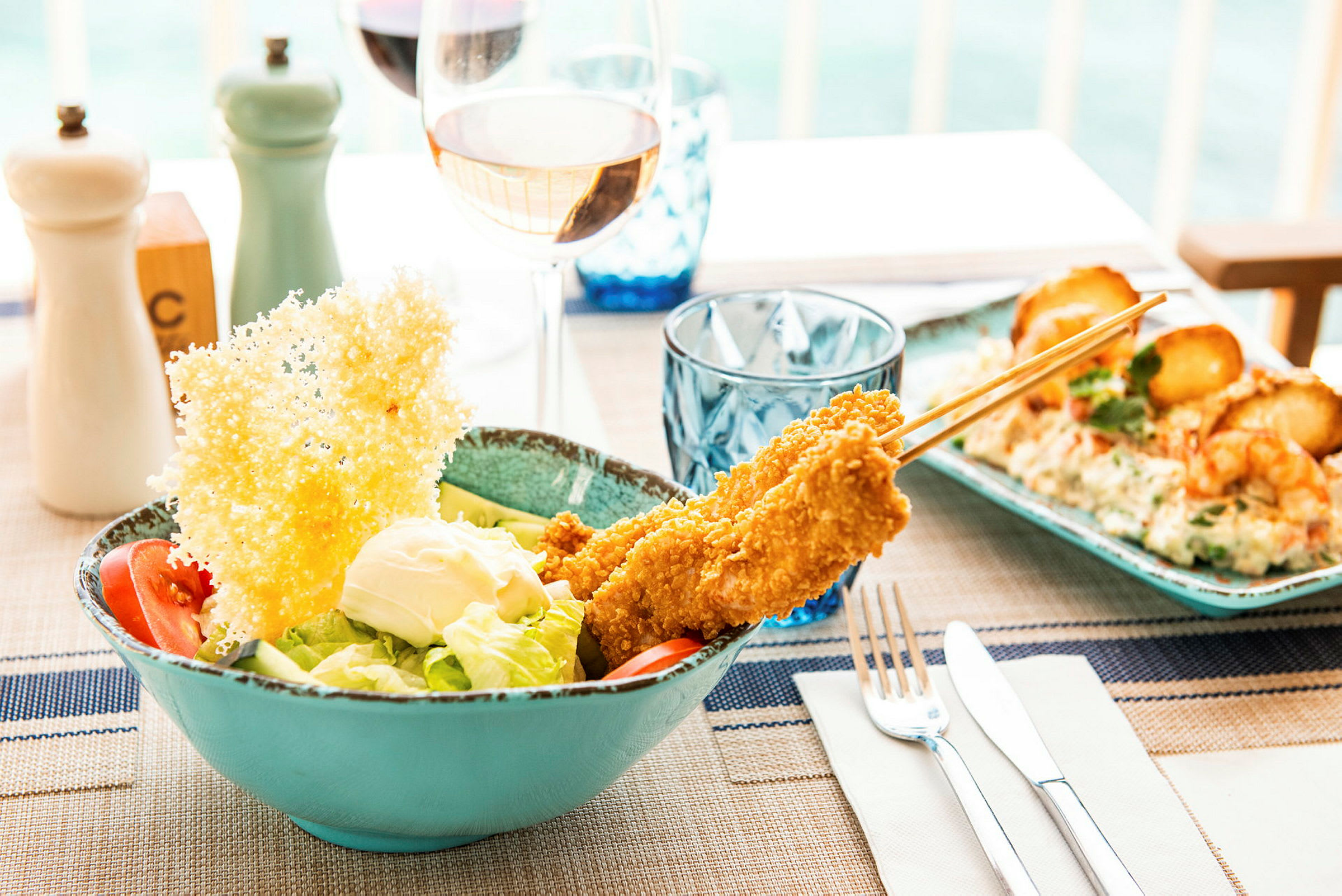 En salat med tomat, salat og dressing toppet med sprø kyllingspyd og et stort parmesanflak på et dekket bord. (AI-generert tekst)