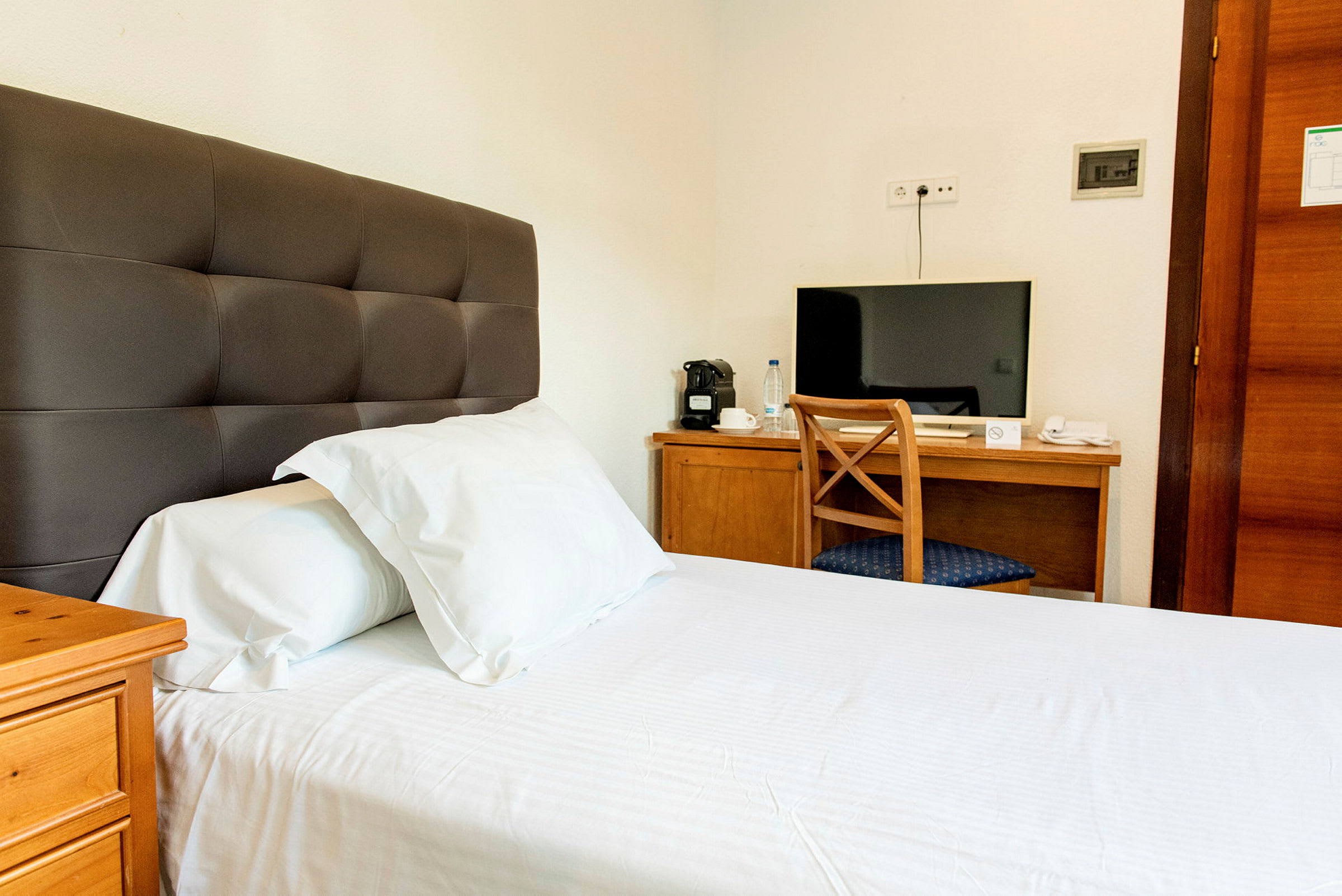 Hotellrom med en seng og et skrivebord med en stol og en TV. (AI-generert tekst)