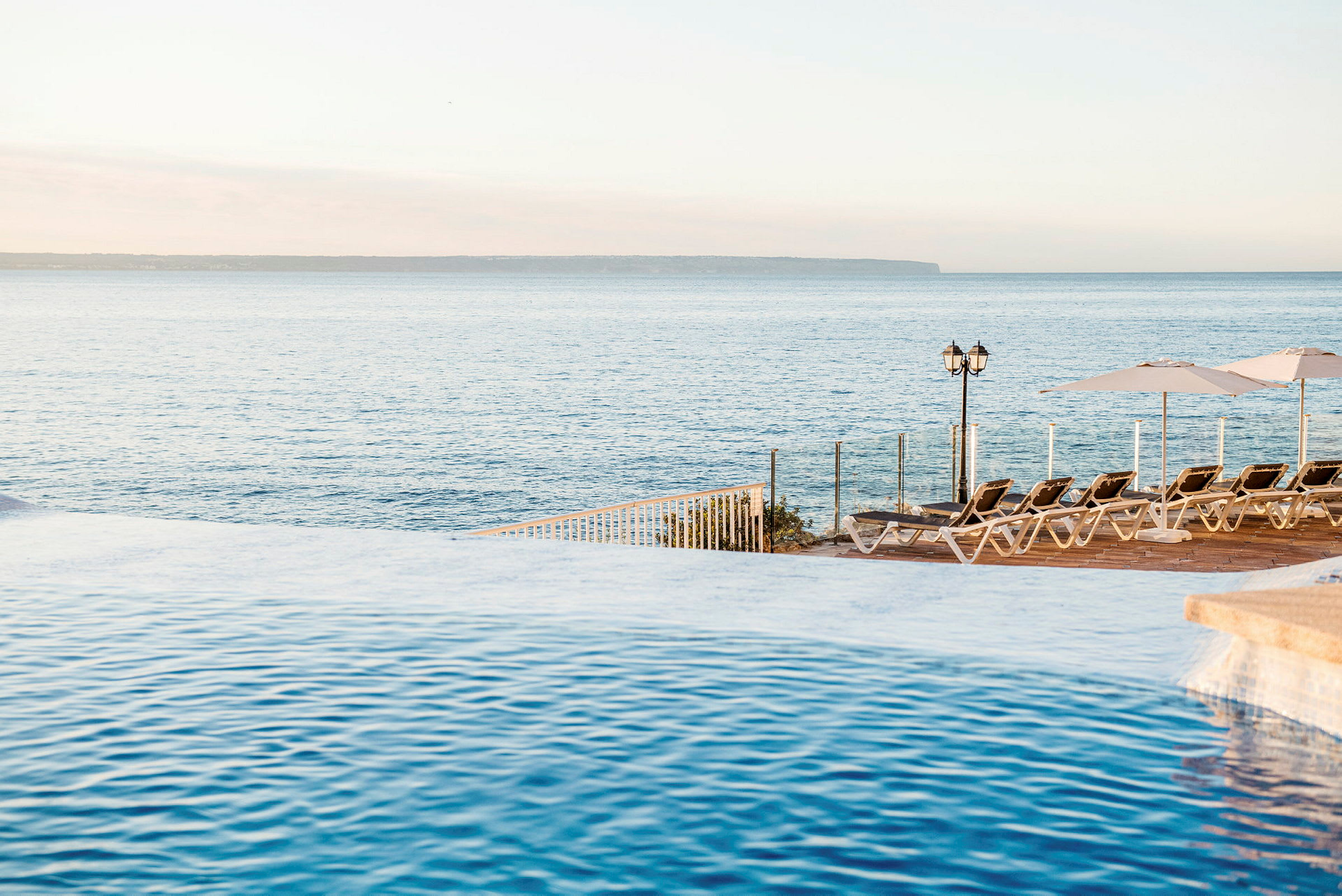 Basseng med utsikt over havet og solsenger på terrasse. (AI-generert tekst)
