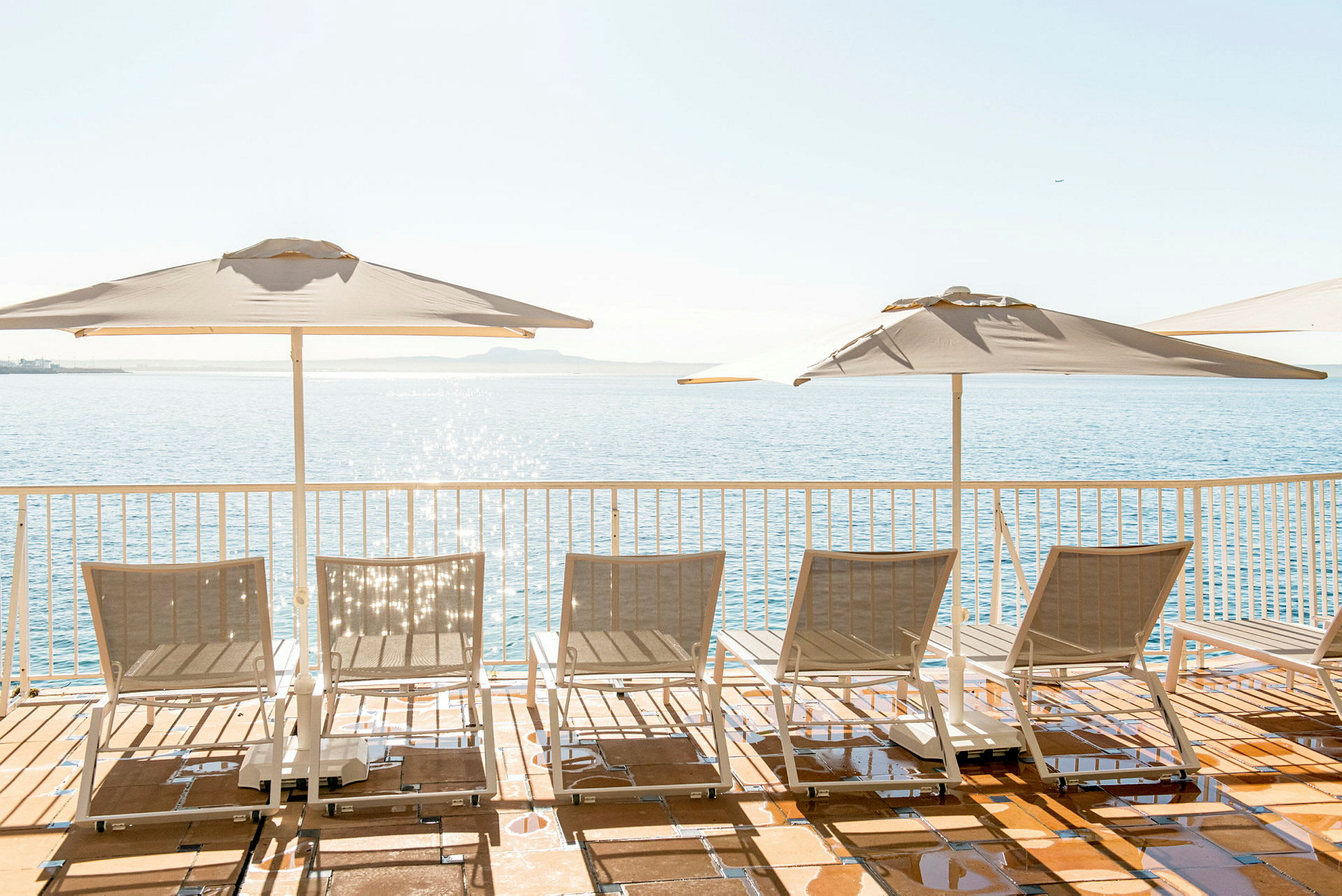 Solstoler og parasoller på en terrasse med utsikt over havet. (AI-generert tekst)