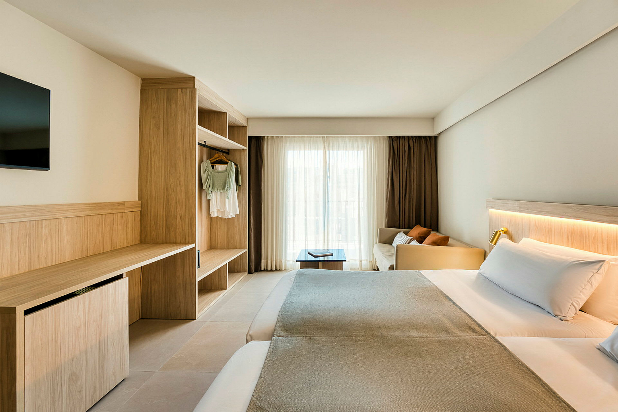 Et hotellrom med dobbeltseng, skrivebord og garderobe. Vinduet er dekket med lyse gardiner. (AI-generert tekst)